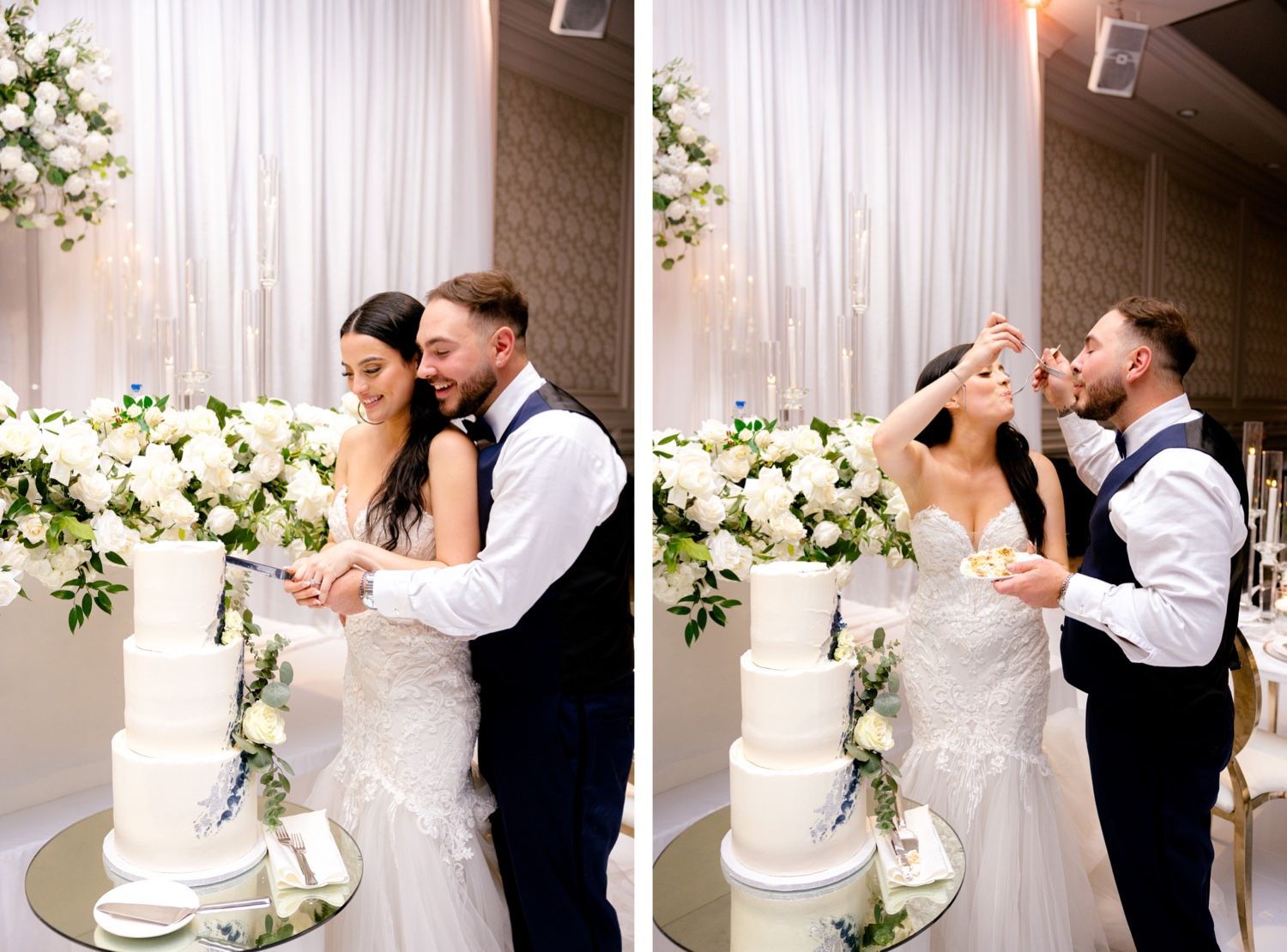 Elegant couple sharing cake cutting moment at wedding reception with white floral backdrop.