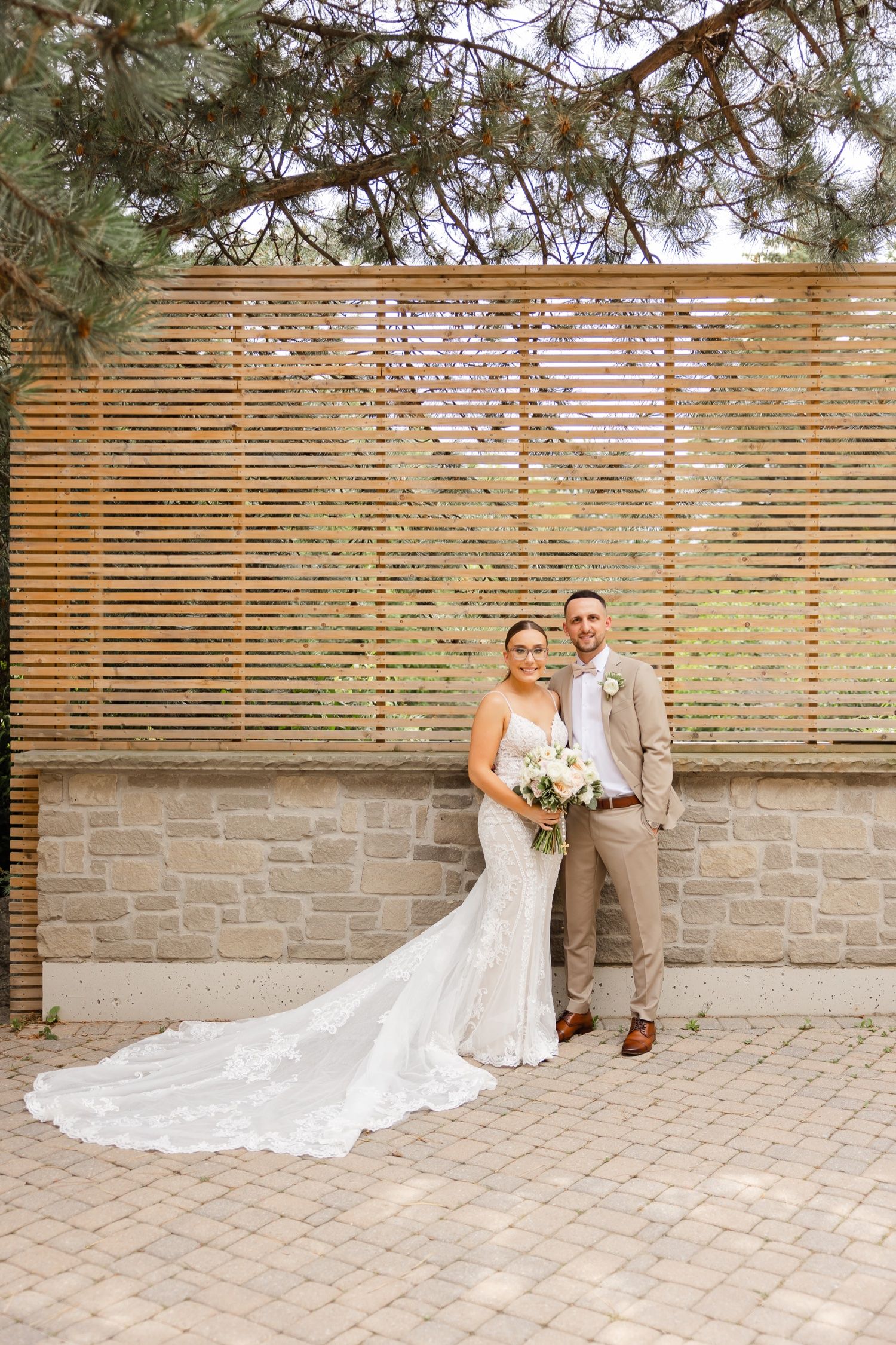 A wedding portrait featuring a couple standing against a modern wooden slat wall with stone base.