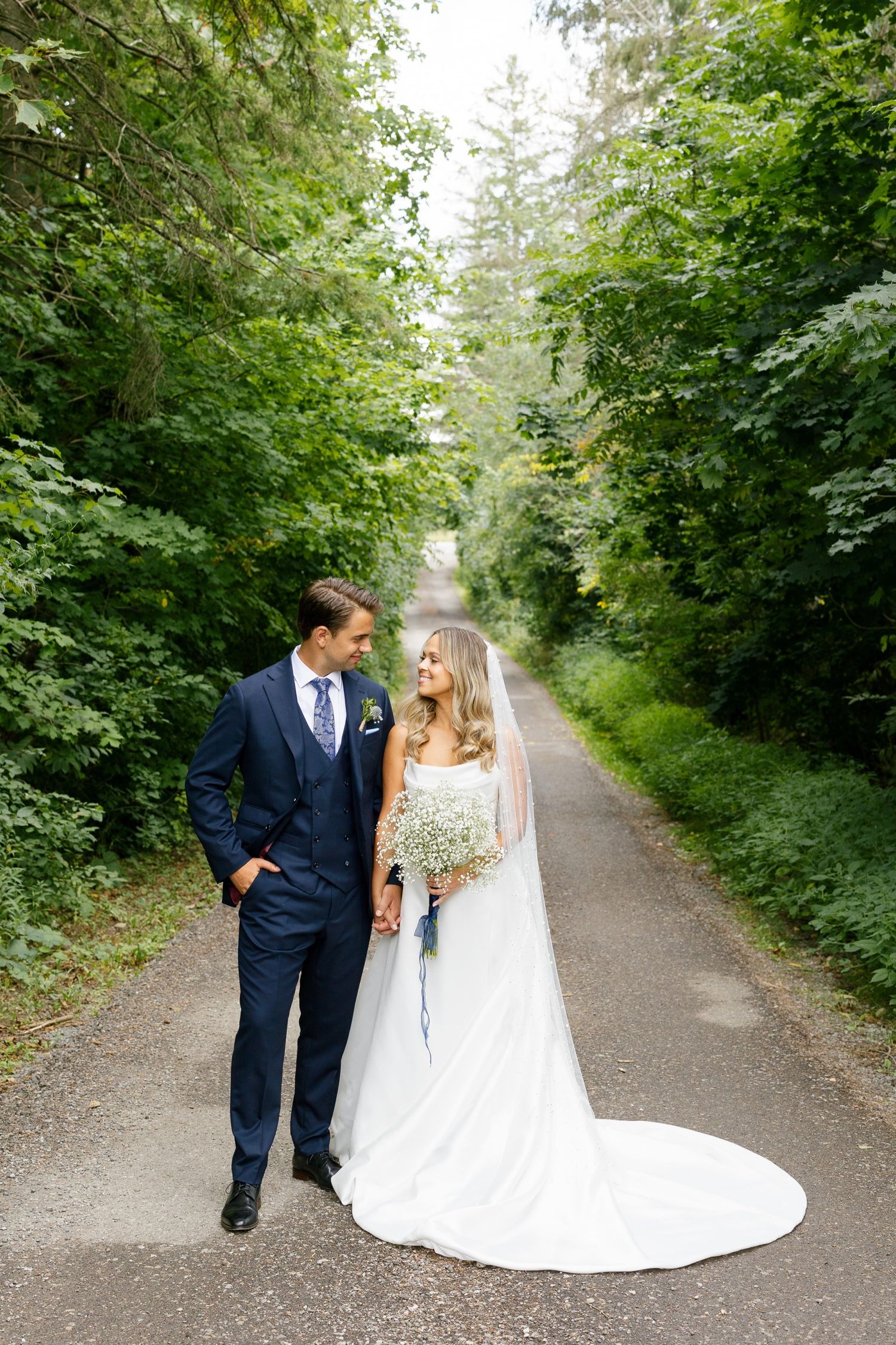 Newlyweds walking together on a serene forest path with trailing white wedding dress.