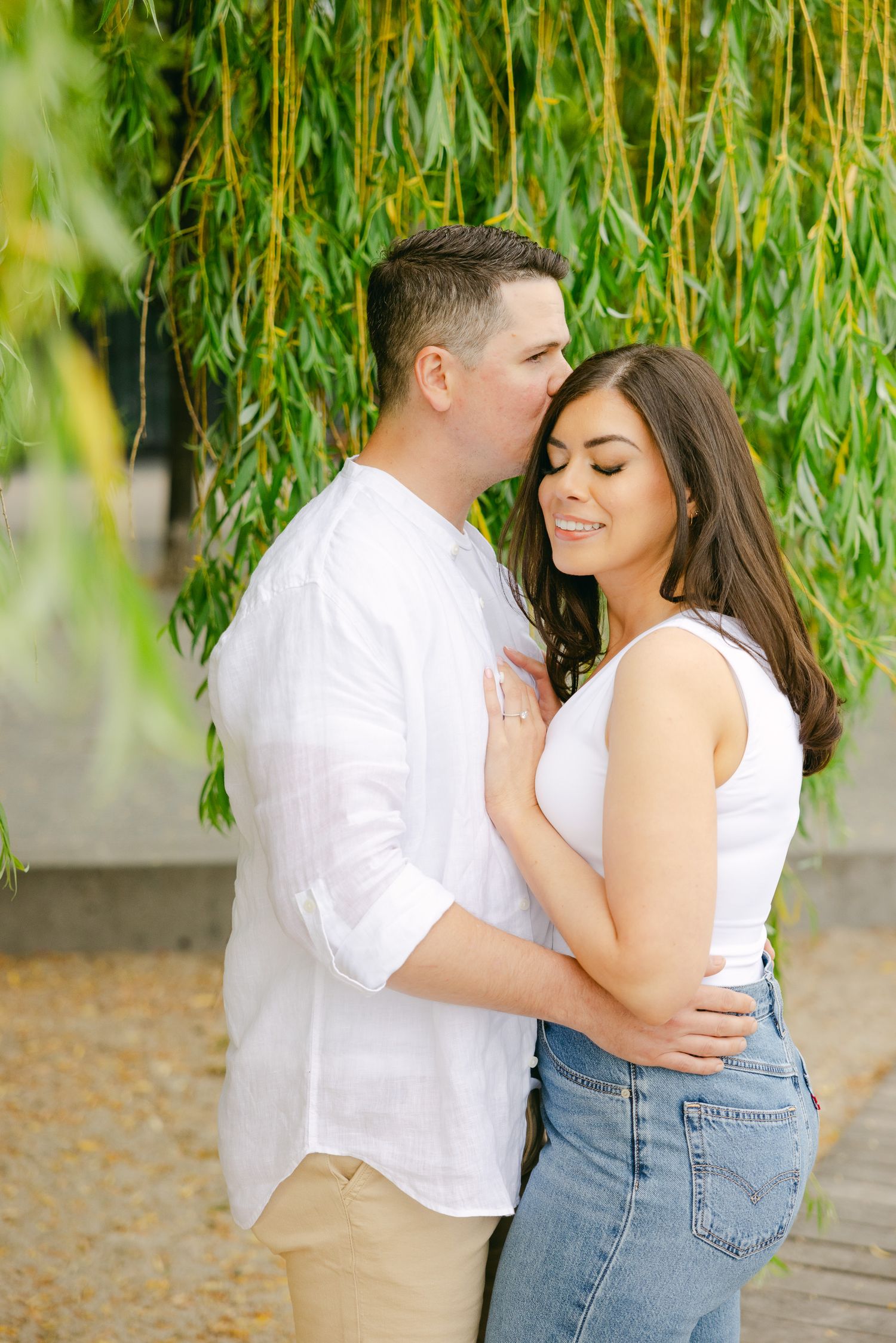 Romantic waterfront portrait of couple sharing intimate moment under willow tree.