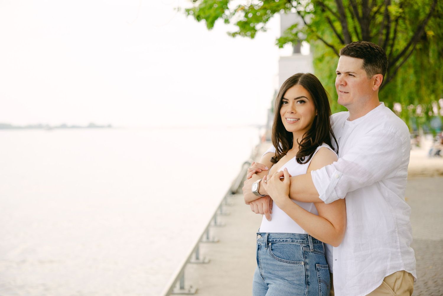 A couple shares a romantic moment by the waterfront on a sunny day.