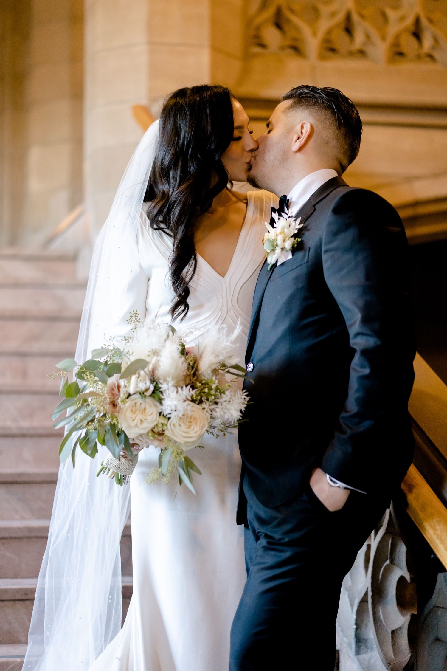 A romantic wedding embrace on an ornate staircase with a beautiful white floral bouquet.