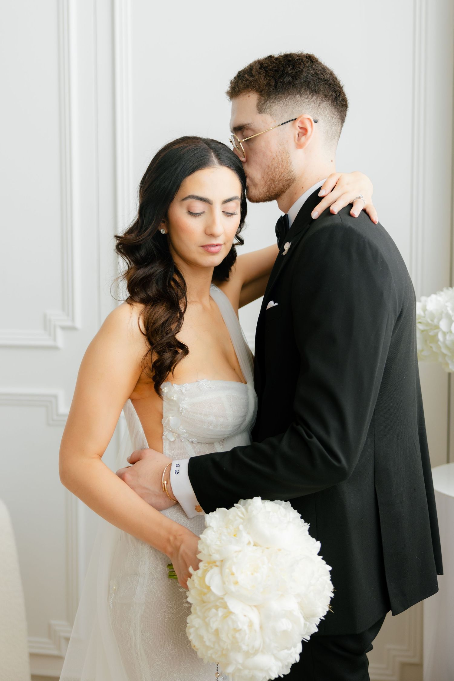 An intimate wedding portrait showing a gentle embrace against classic white wall paneling.