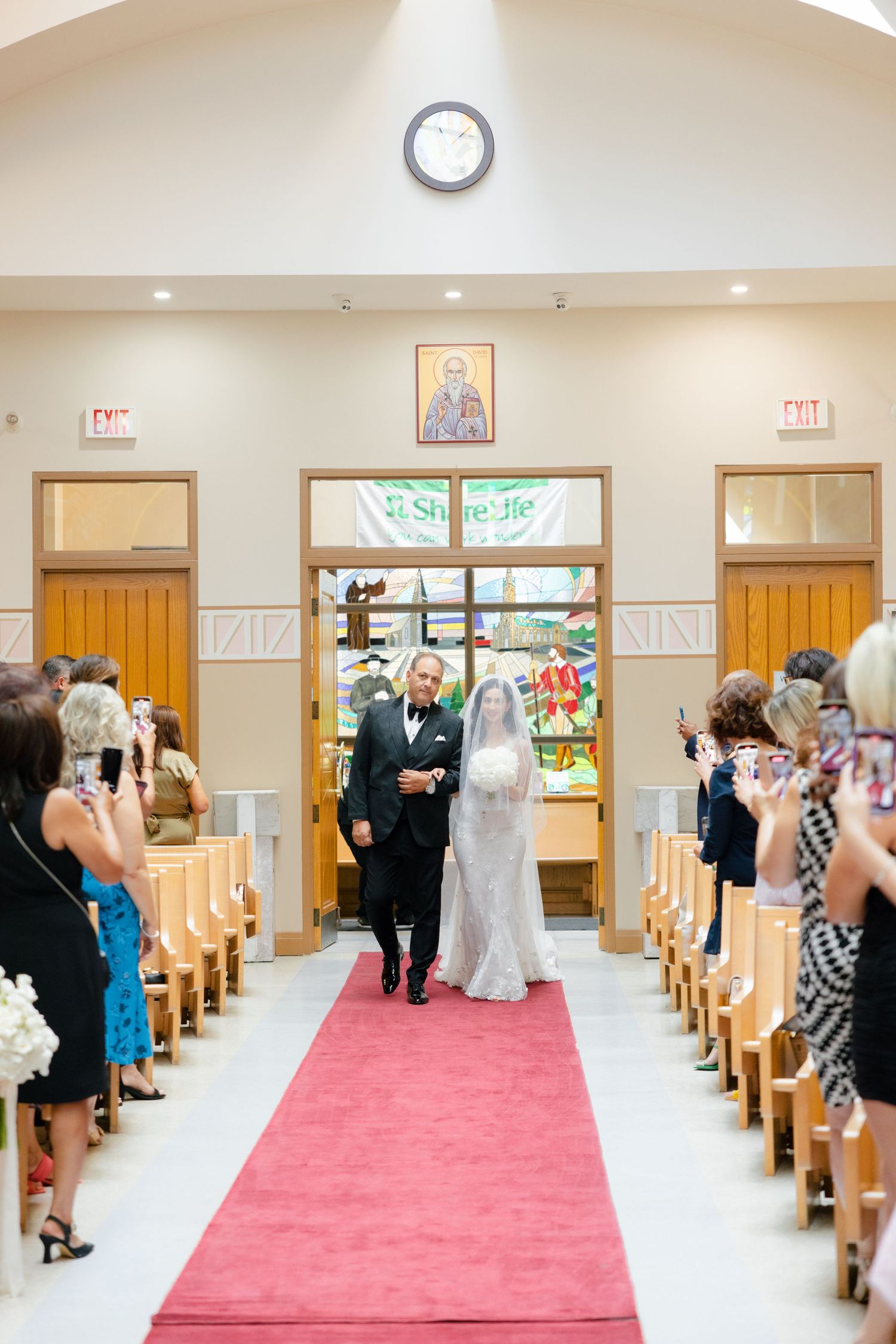 Church wedding ceremony with guests watching couple walk down red-carpeted aisle.