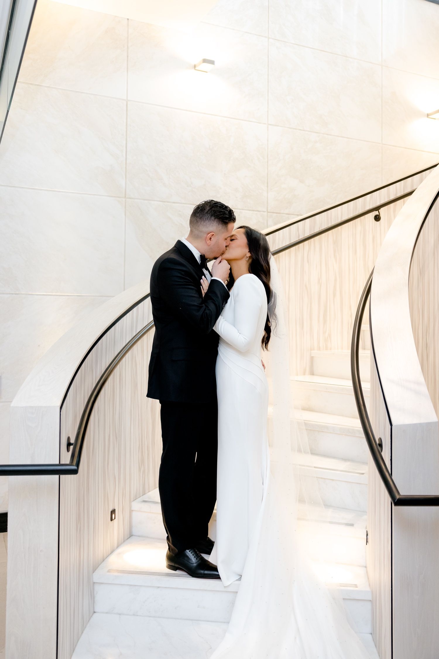 Romantic wedding portrait of couple sharing intimate moment on white marble staircase.