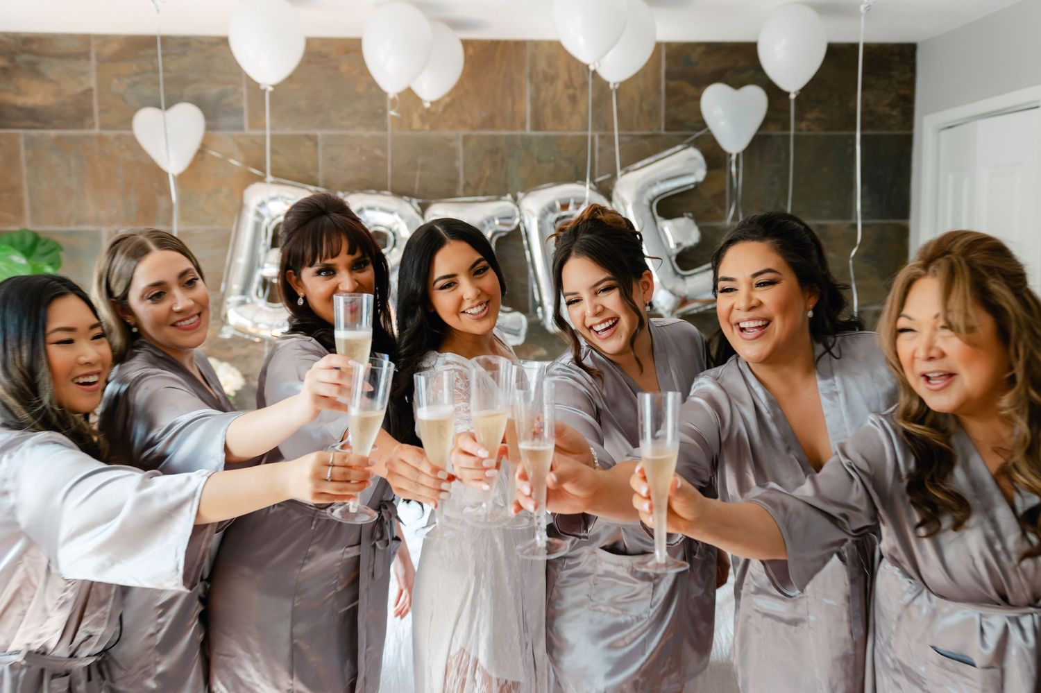 Bridesmaids in matching gray robes raise champagne glasses for a celebratory toast.
