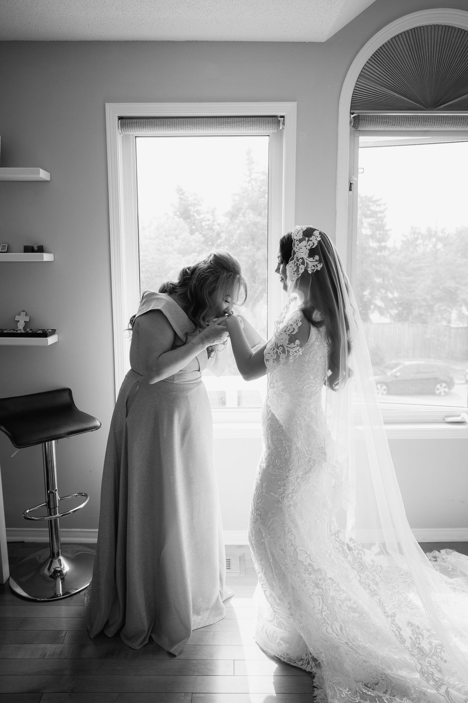 Black and white emotional moment during wedding preparations by sunlit windows.