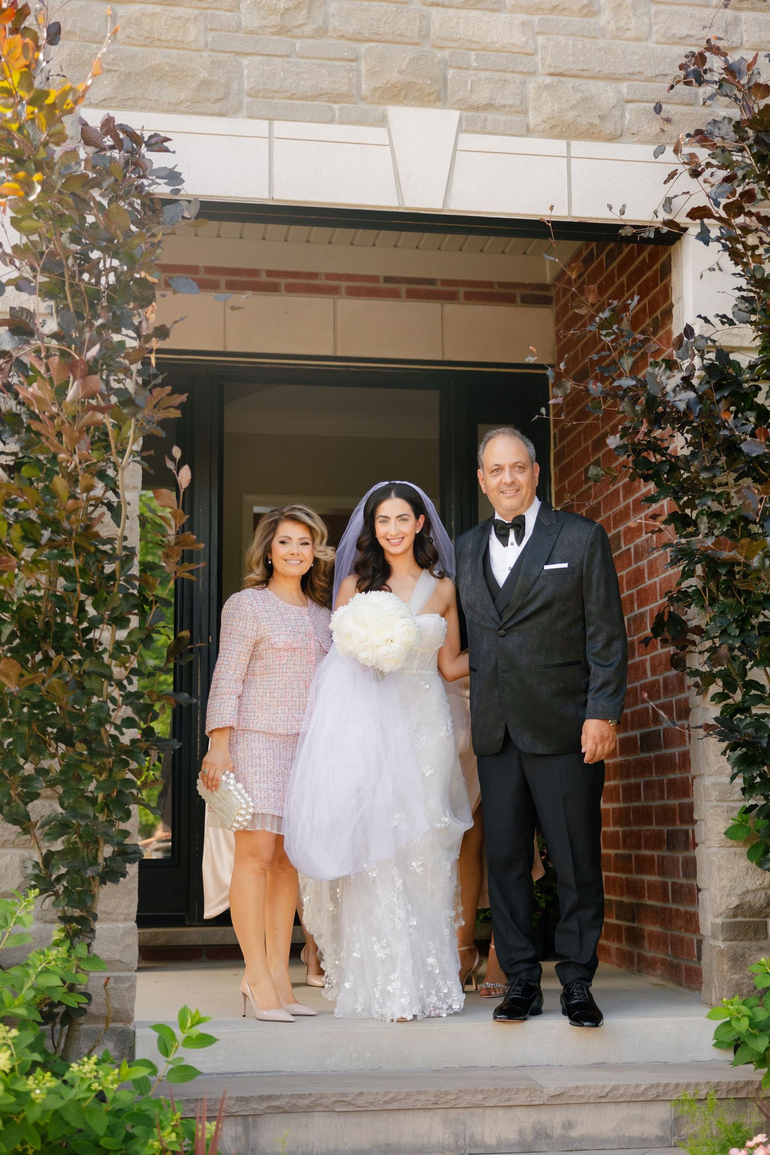 Wedding portrait outside a brick entrance with family members on stone steps.