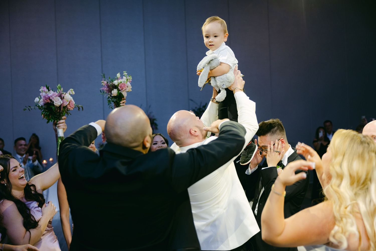 A small child is lifted high in the air during an energetic wedding celebration.