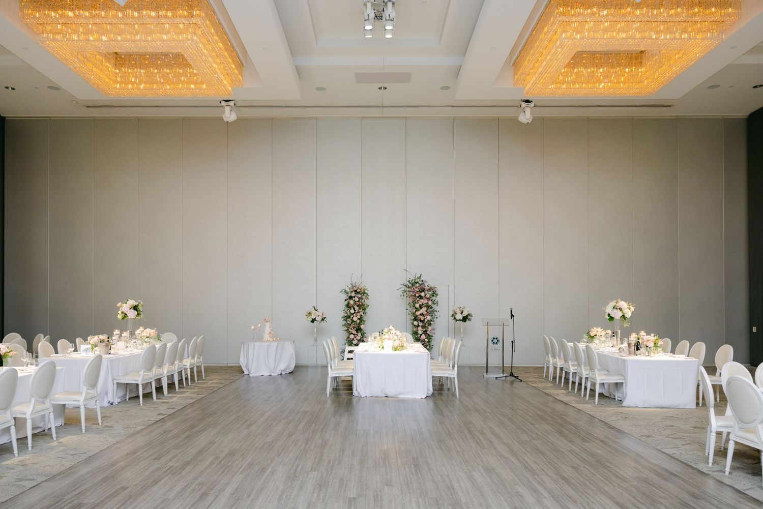 Elegant wedding venue setup with white chairs and floral arrangements under ornate gold chandeliers.