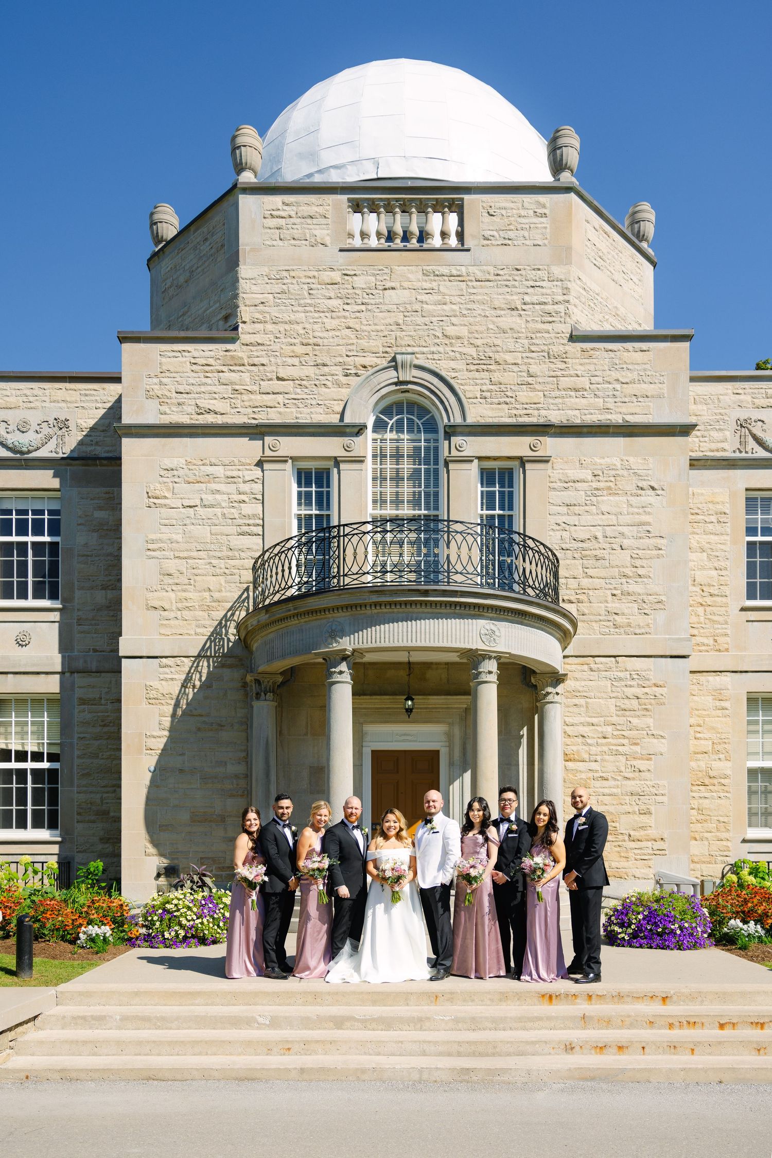 Wedding party poses on steps of historic limestone building with domed roof.