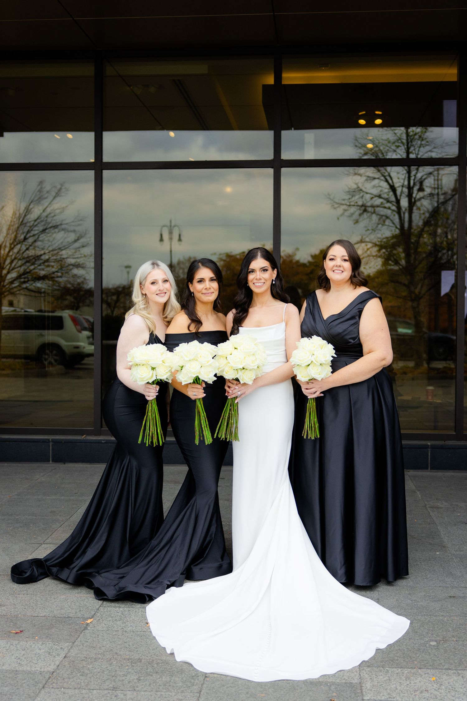 Bridal party in navy dresses holding white bouquets poses with bride in flowing white gown.