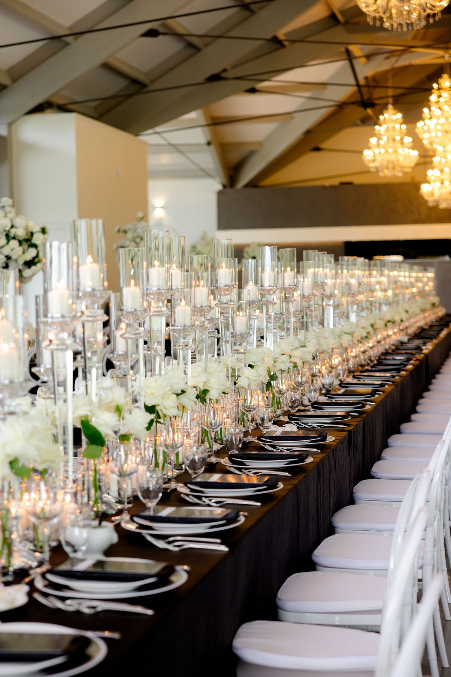 Long wedding reception table with black linens, white chairs, and crystal candleholders stretching into the distance.