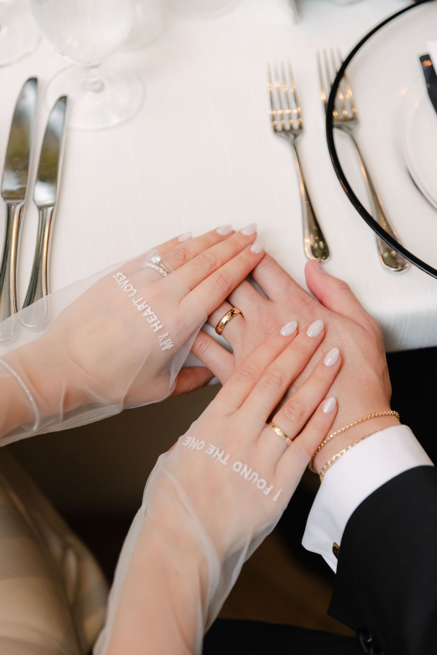 Close-up of wedding rings and hands on a formal table setting with silverware.