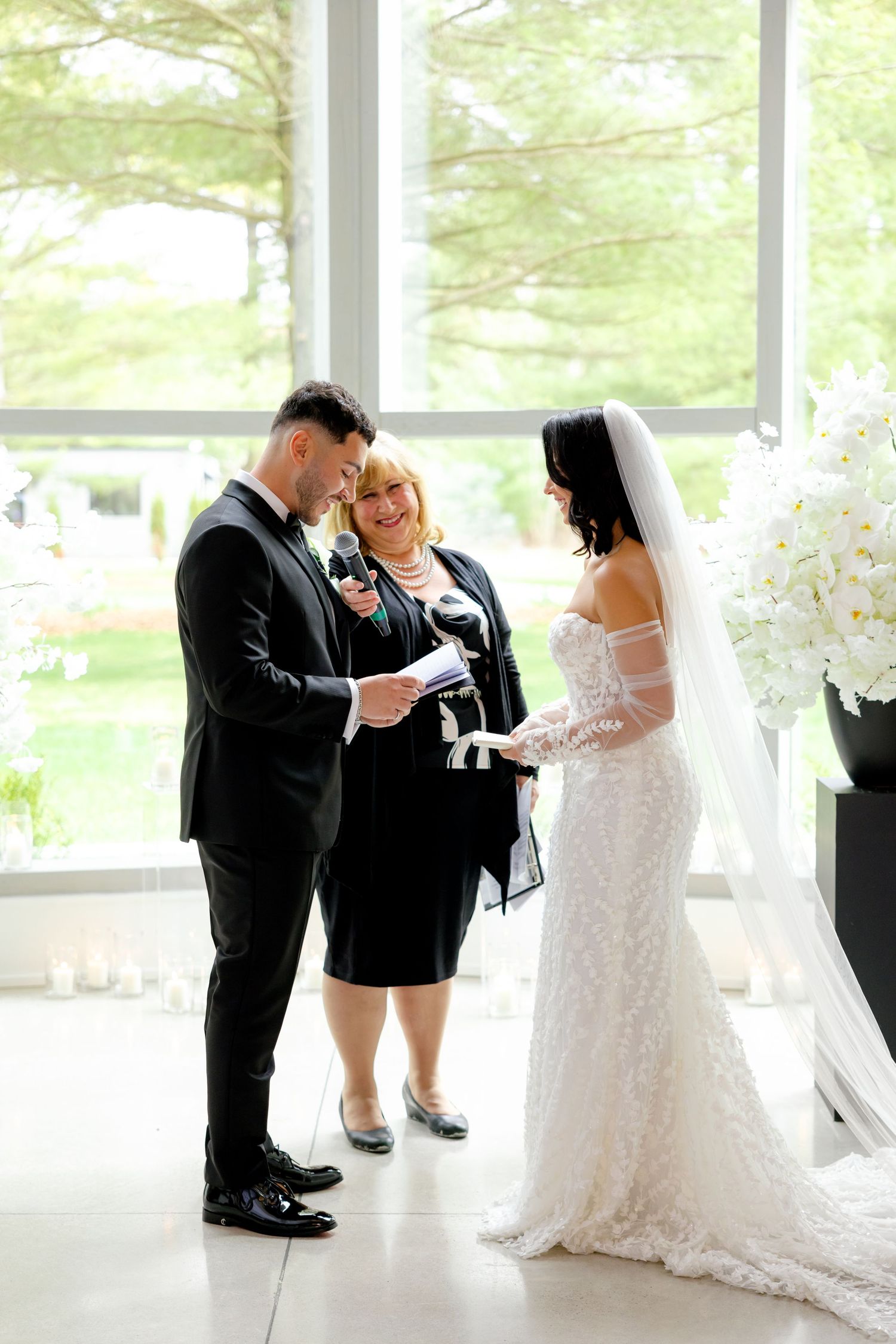 Wedding couple exchanging rings during intimate ceremony with officiant in sunlit room.