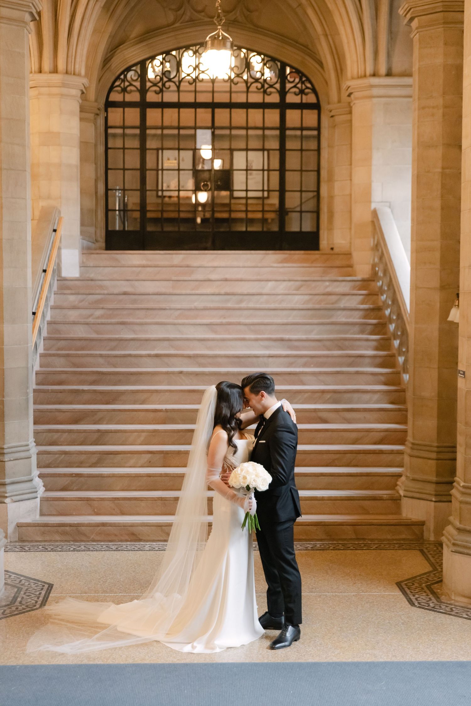 A romantic wedding moment on grand marble stairs with elegant arched architecture and wrought iron details.