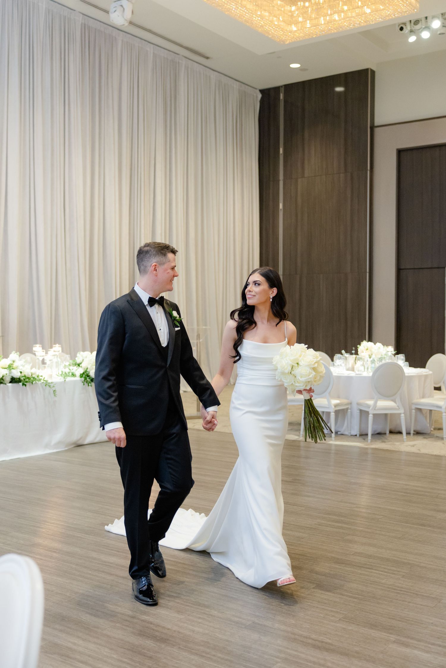 Elegant wedding moment in modern venue with white drapery and floral arrangements.
