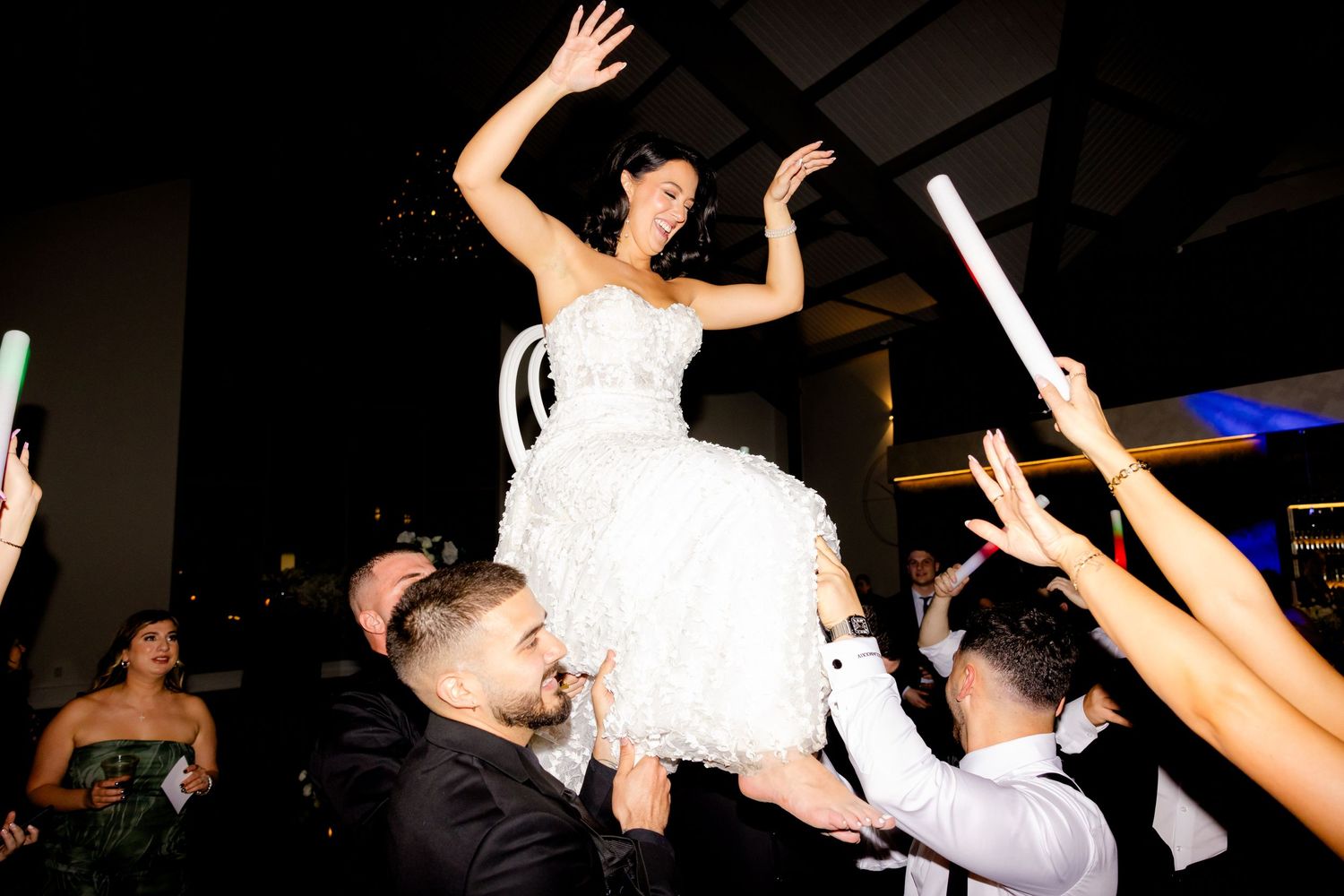 Bride in white dress being lifted by wedding guests during festive dance celebration.