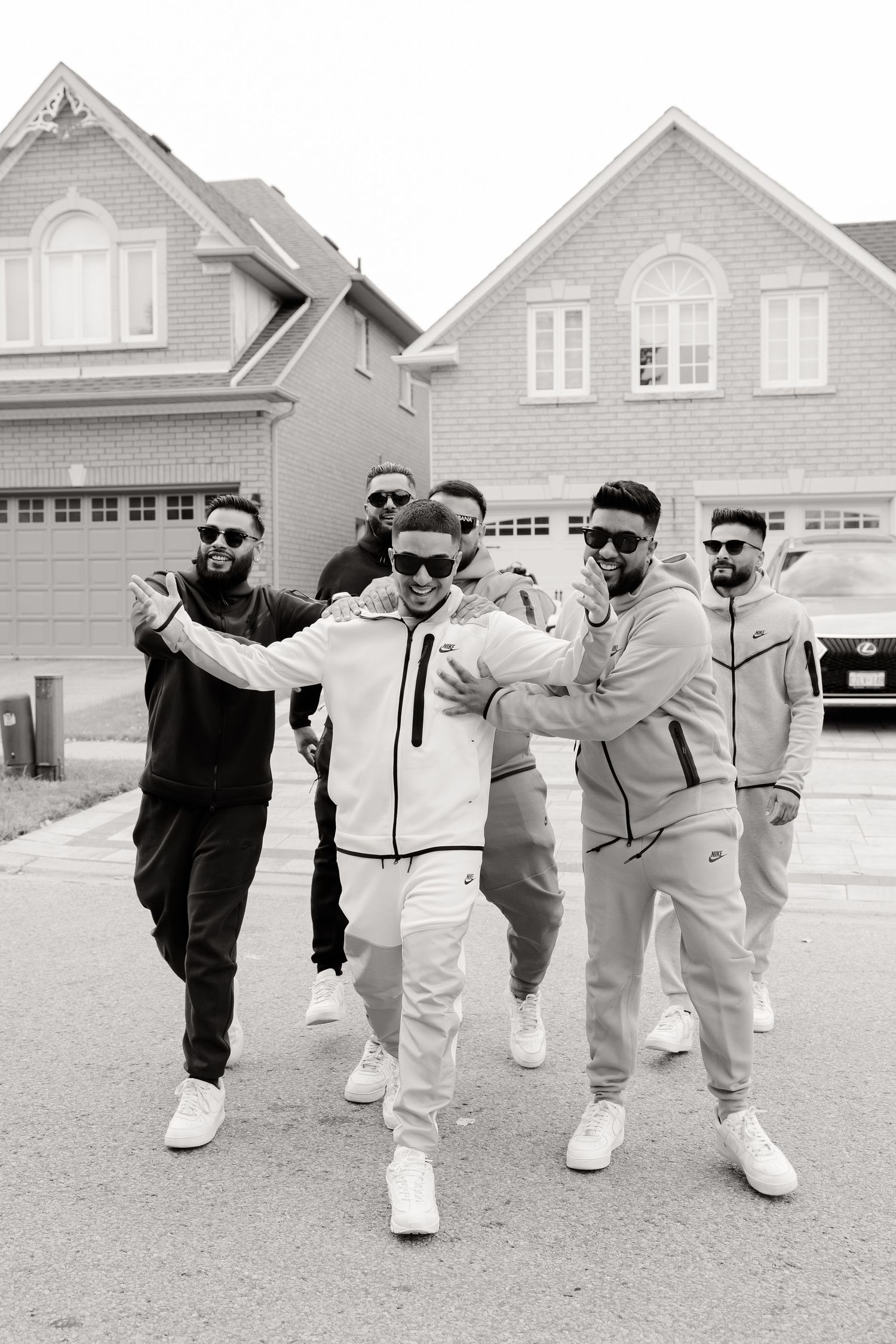 Black and white photo of a group in athletic wear posing playfully outside suburban homes.