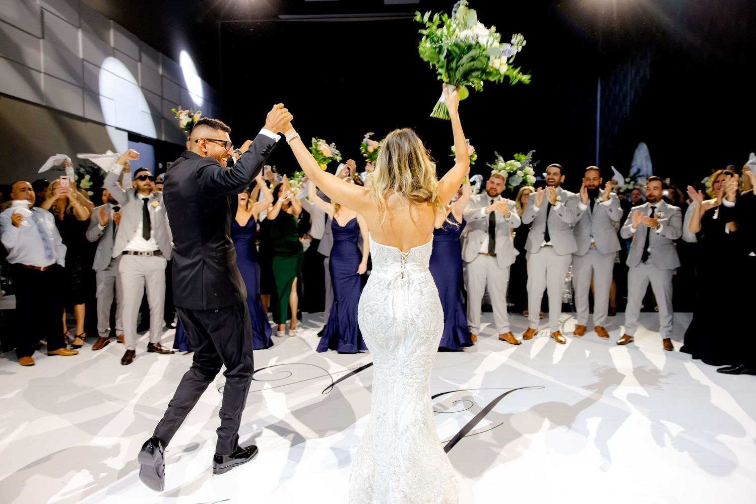 Joyful newlyweds celebrate on the dance floor while guests cheer in the background.