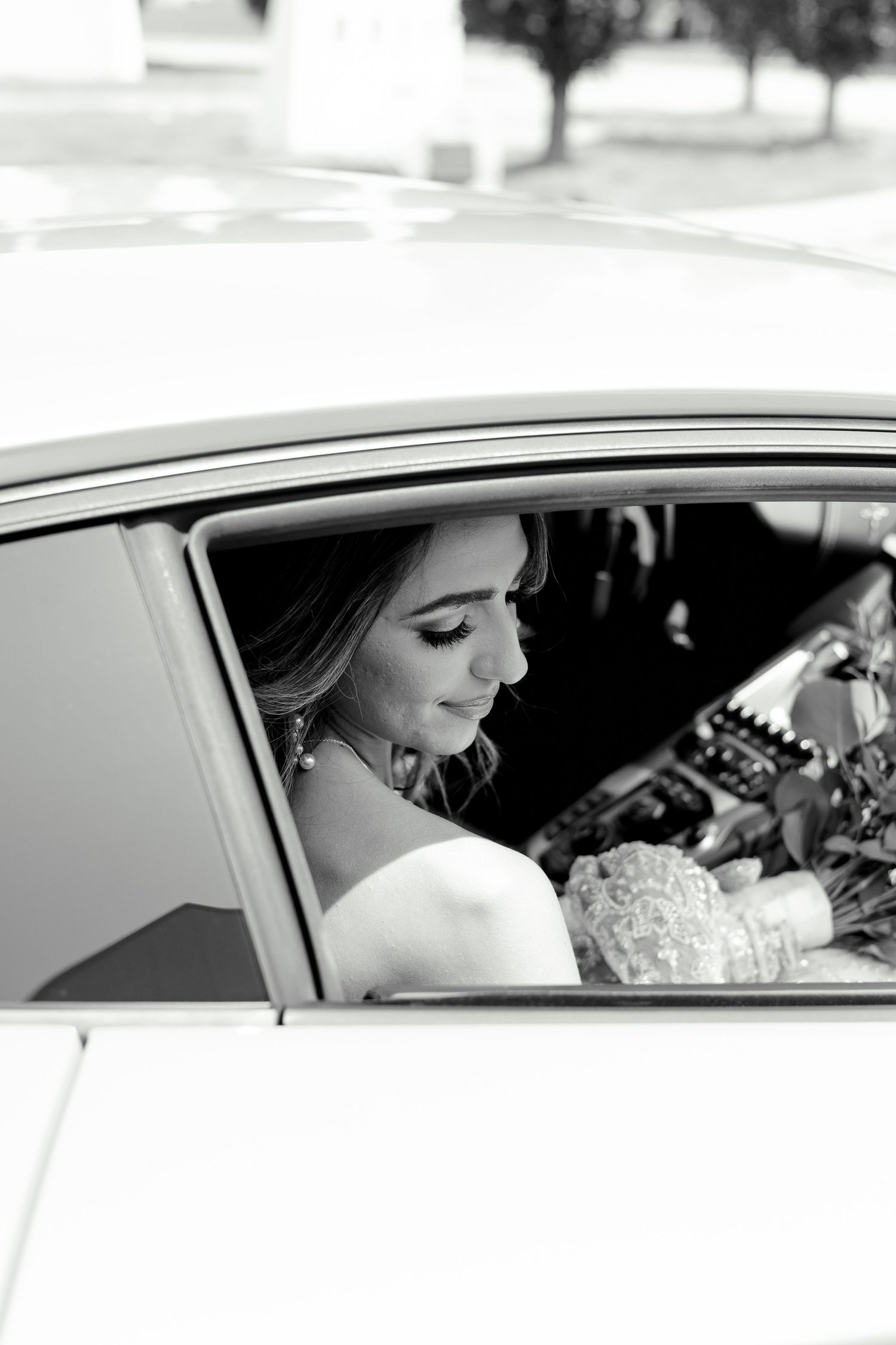 Black and white portrait of couple in wedding attire inside luxury car.