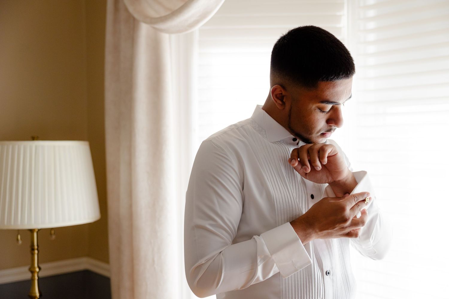Person in formal white shirt buttoning cuffs in elegant room setting.
