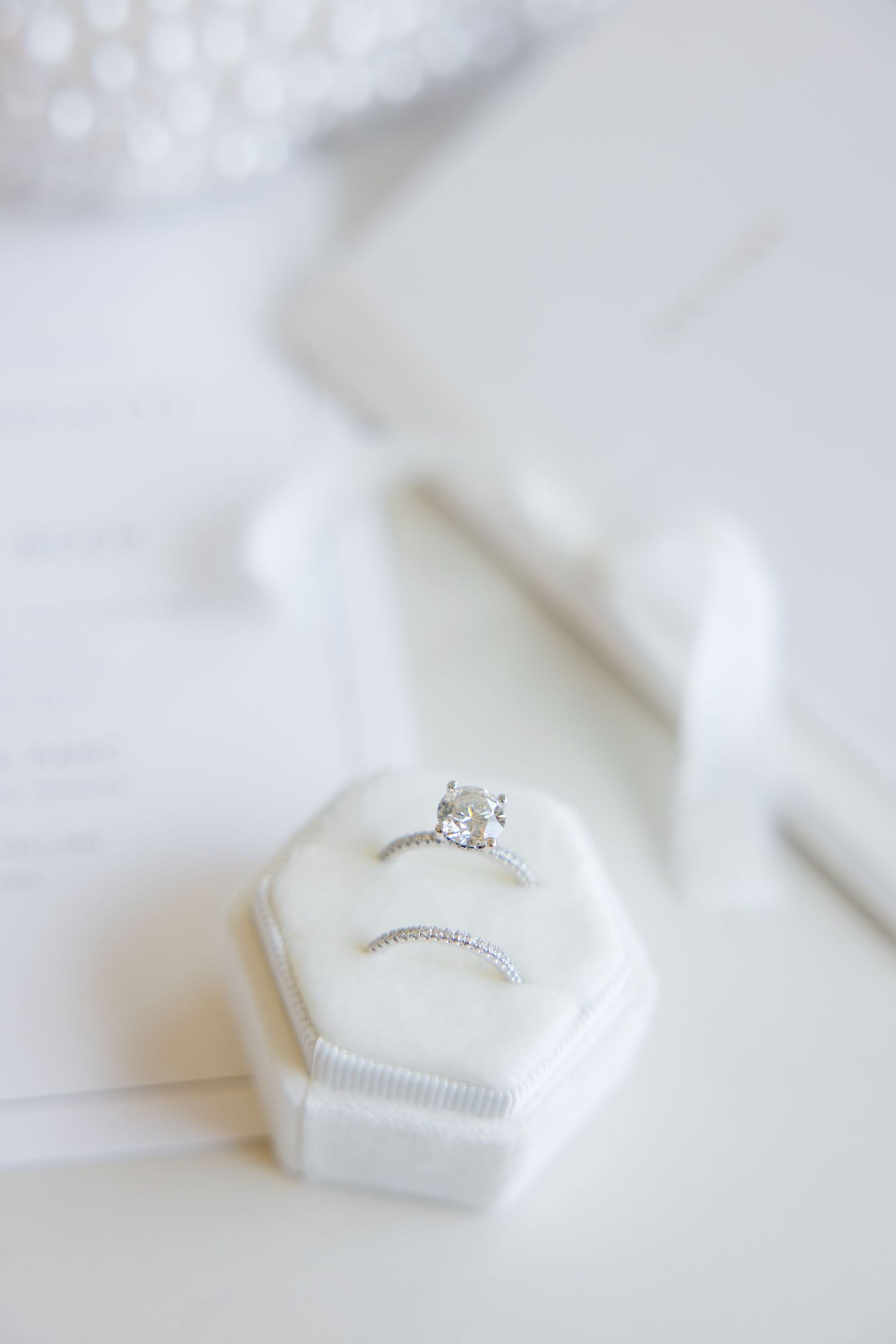 Diamond engagement ring in white hexagonal ring box with soft bokeh background.