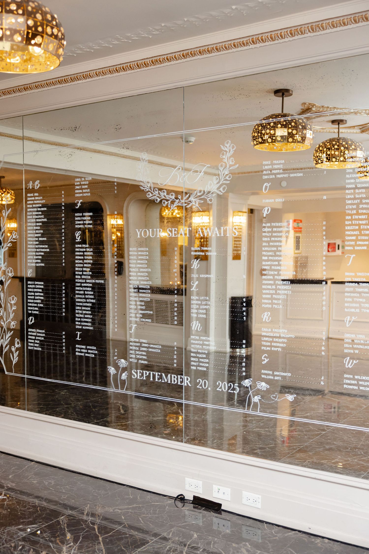 Elegant wedding seating chart displayed on glass panels with white text and floral designs in a luxurious venue.
