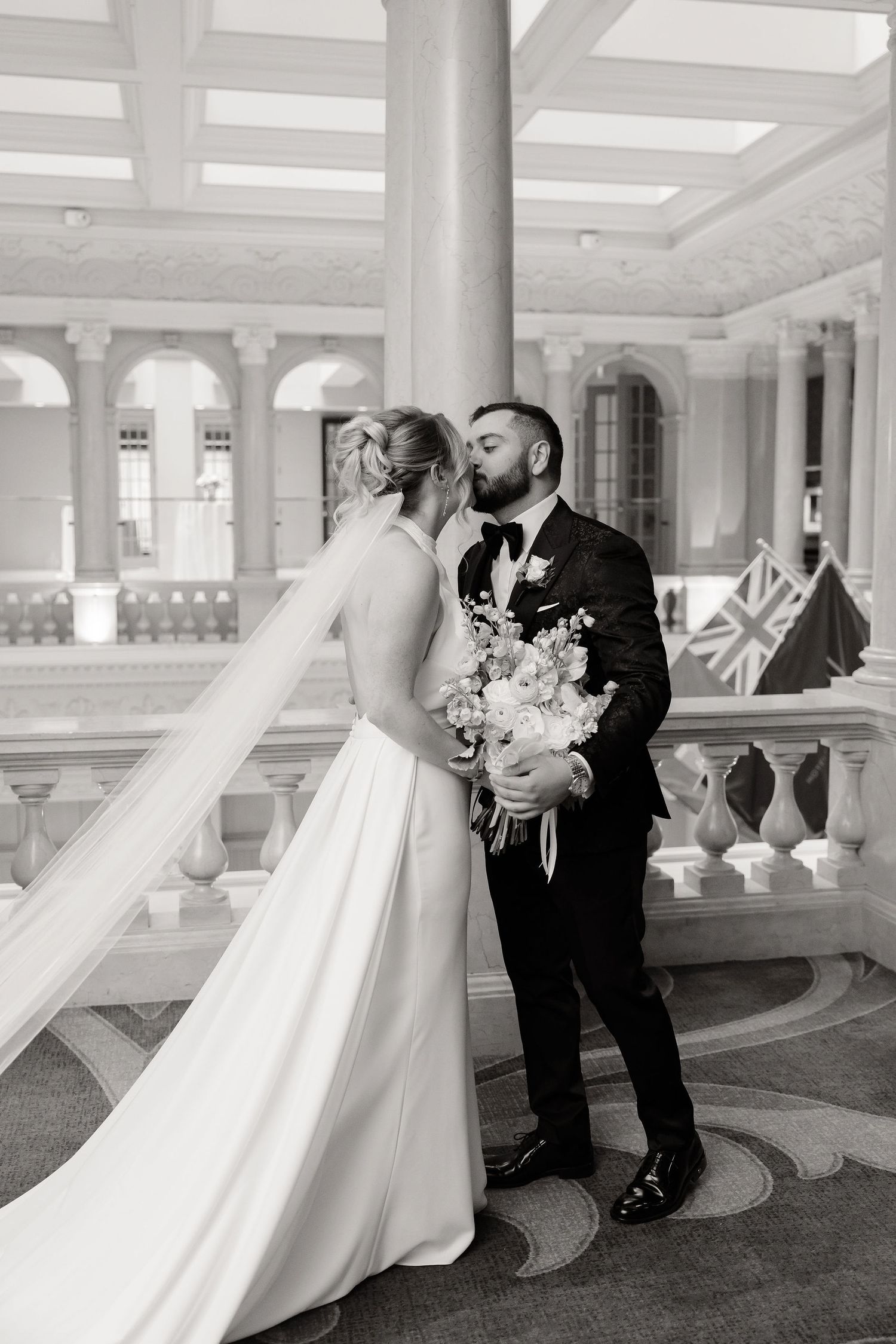 Black and white photos of a couple's first look in an ornate hallway with columns.