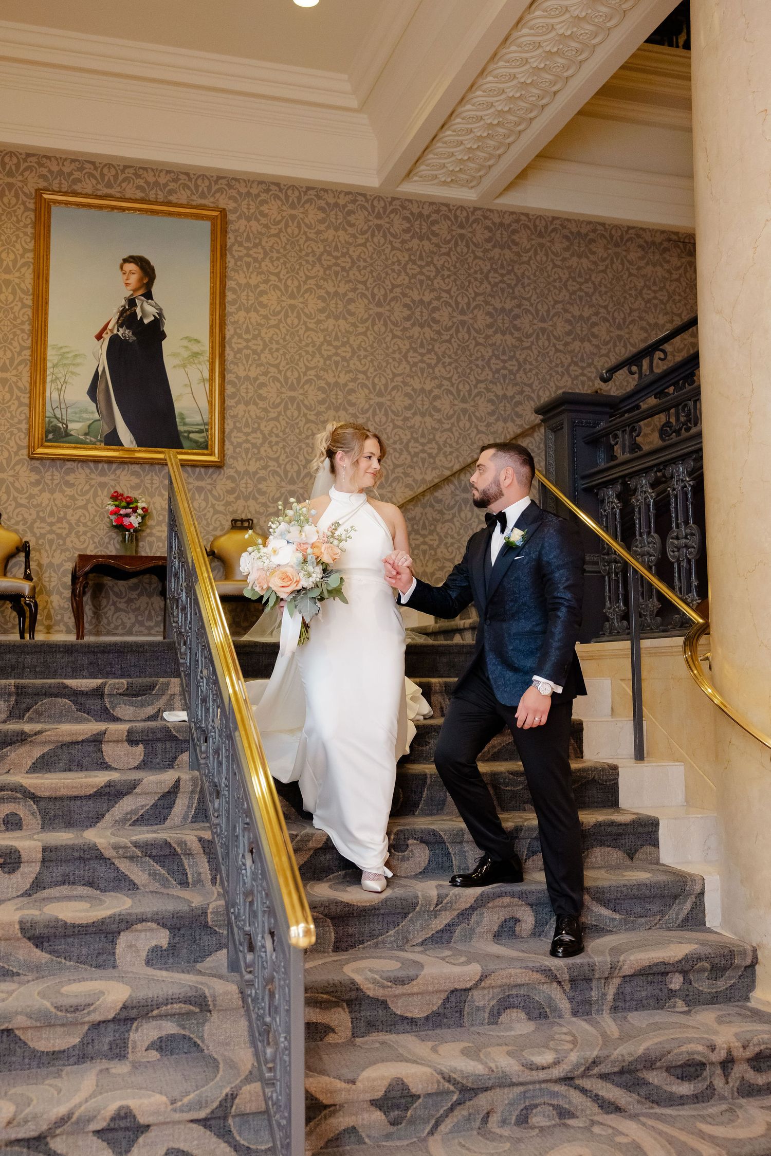 A wedding couple shares a playful moment on carpeted stairs in an elegant interior.