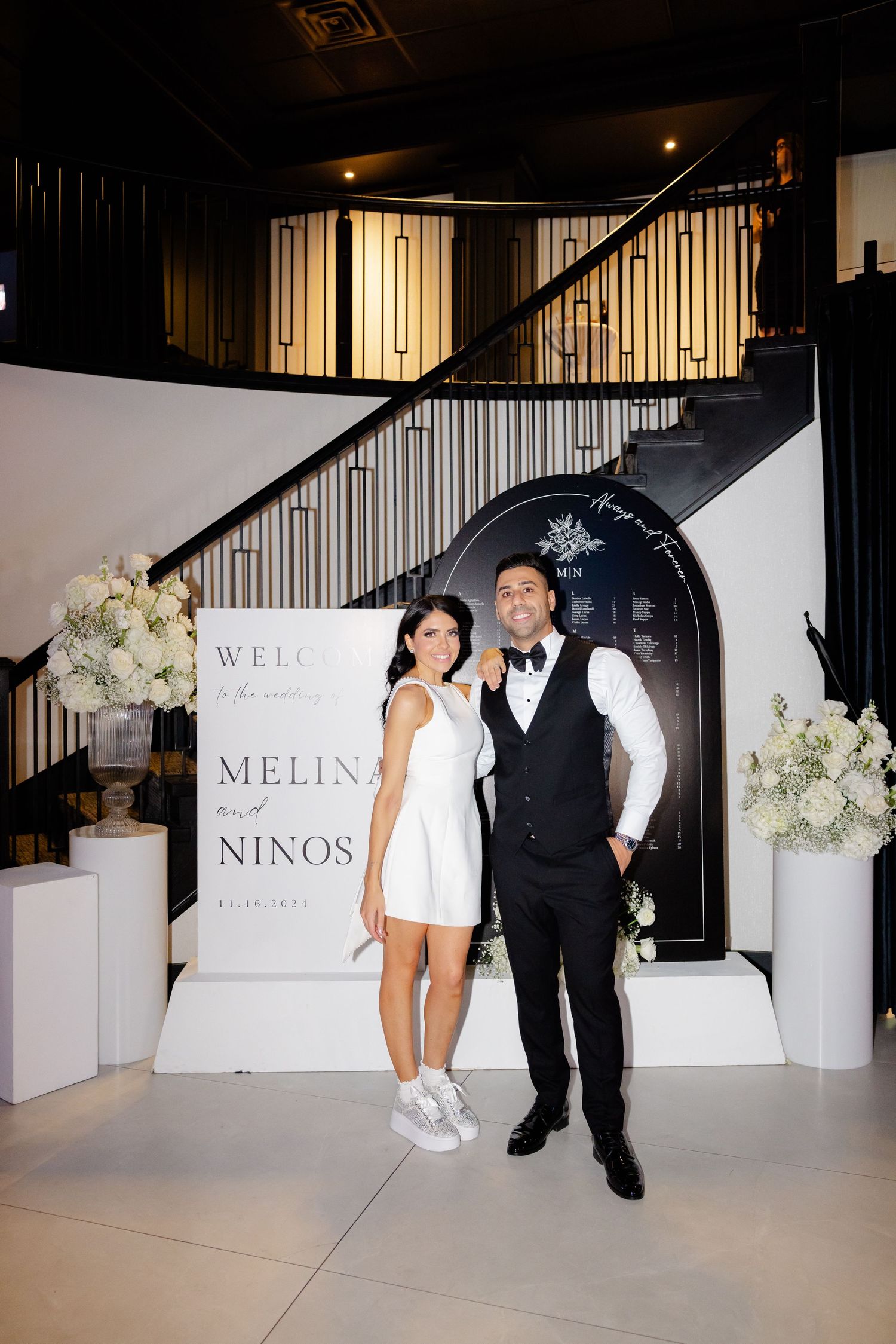 Formal couple poses in front of elegant black and white wedding welcome display.