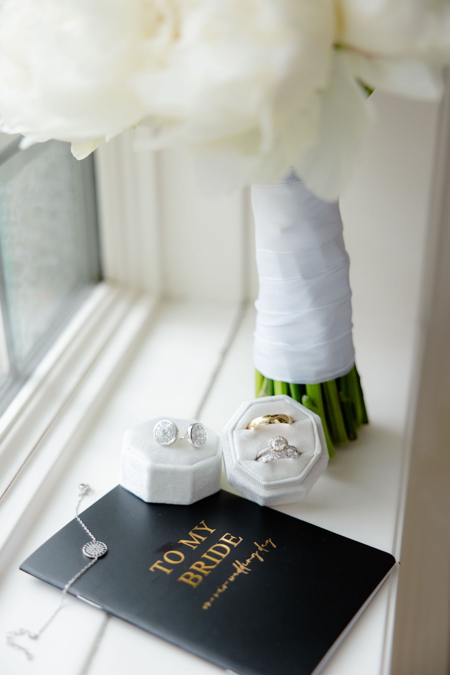 Close-up of wedding jewelry and bridal book arranged with white floral bouquet.
