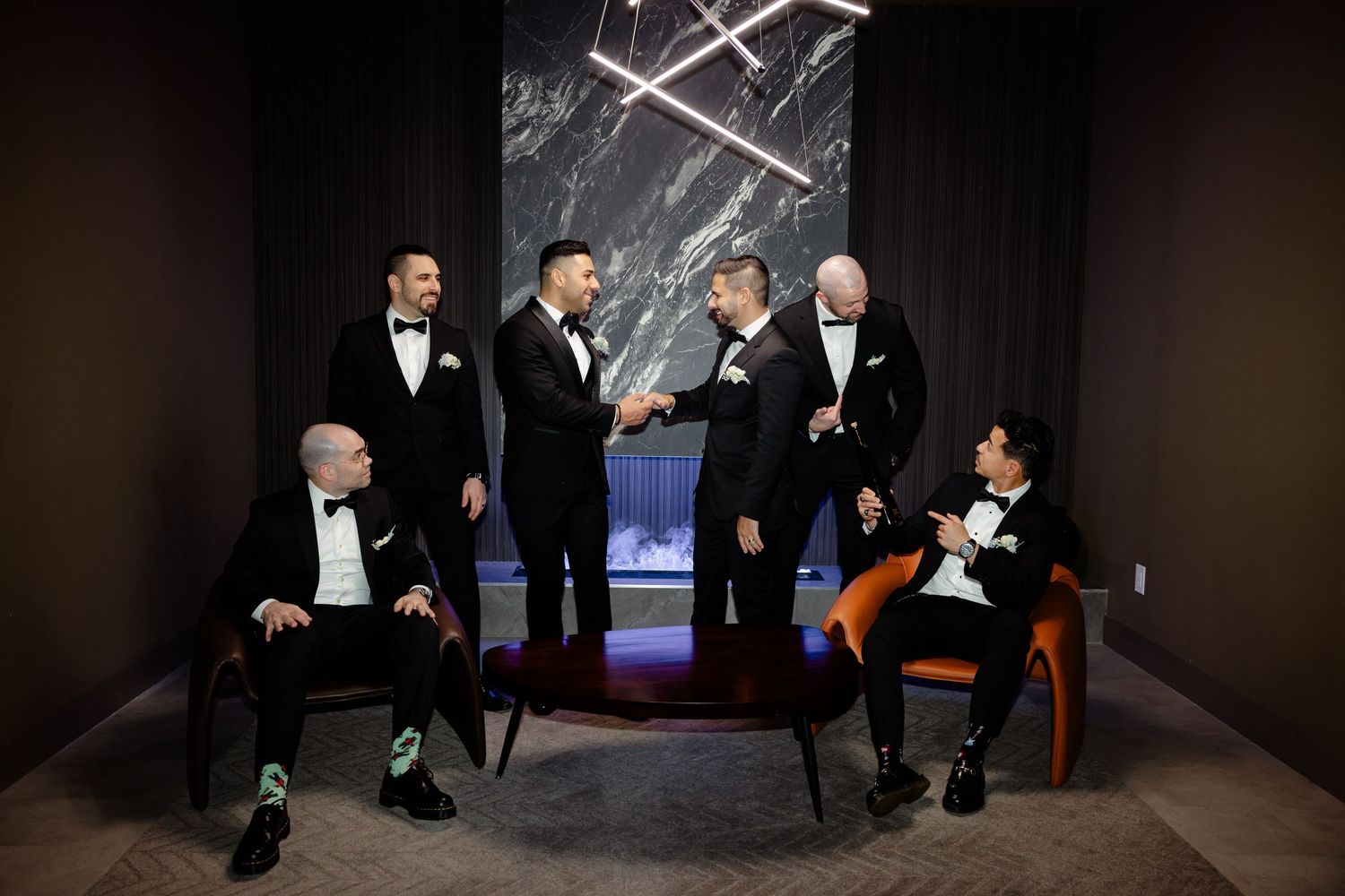 Wedding party members gathered in formal attire against modern backdrop with lighting installation.
