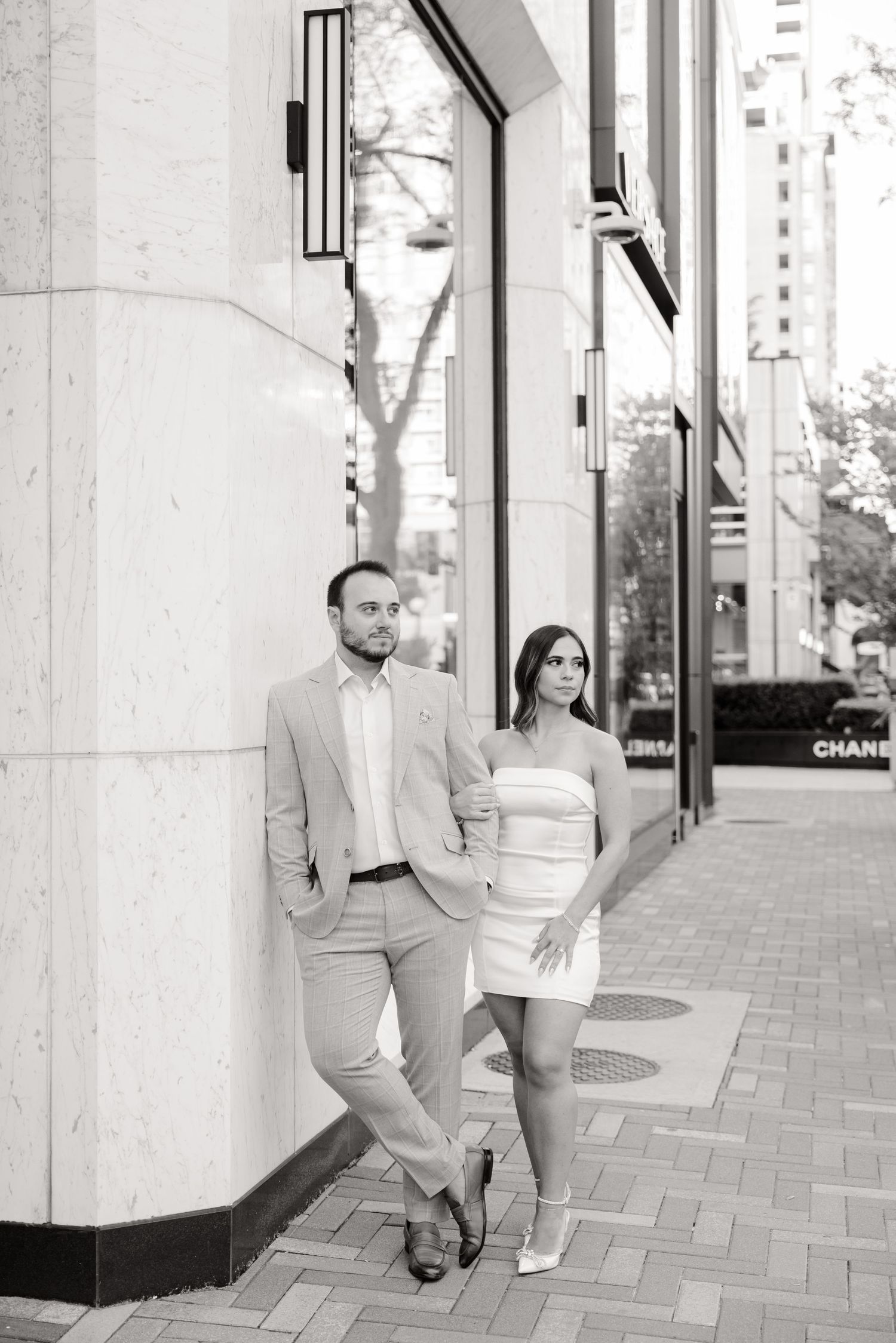 Black and white photo of a couple in formal attire standing together on a city street.