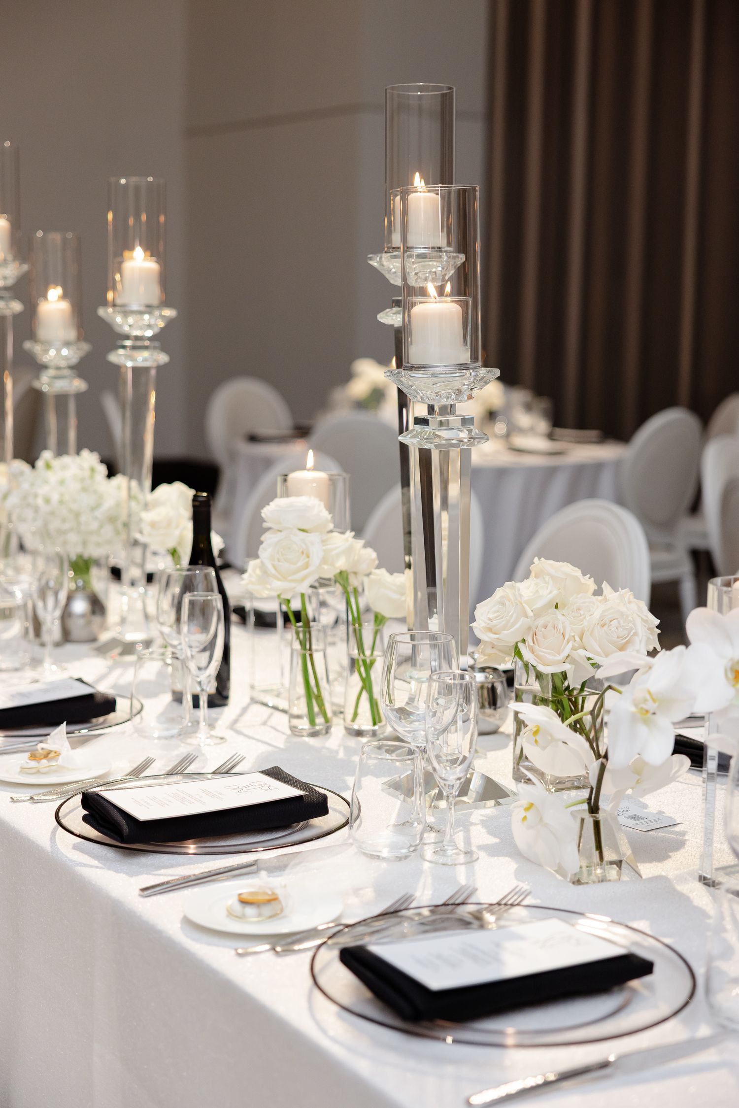 Elegant wedding table setting with white flowers, glass candle holders, and black and white place settings.