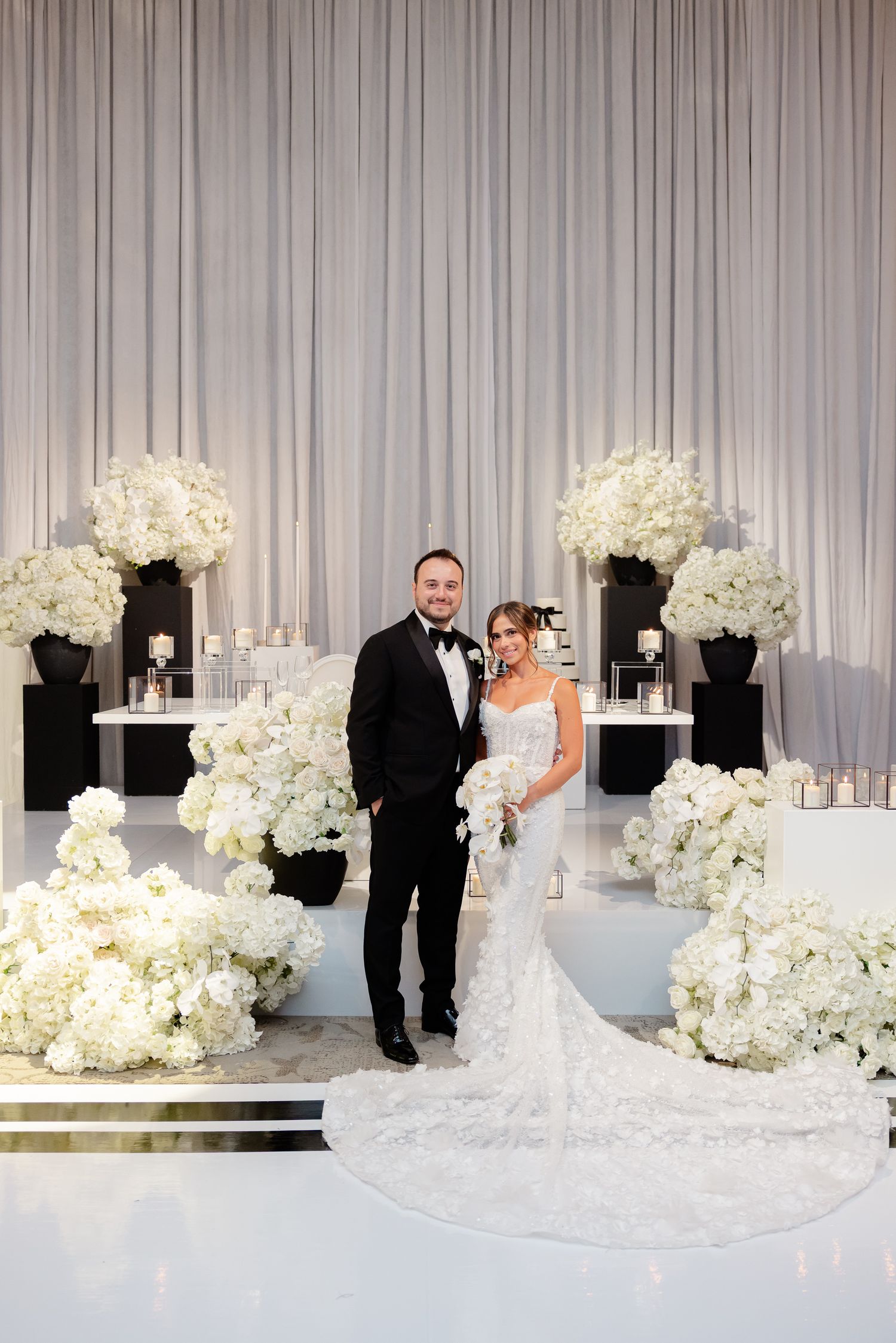 An elegant wedding ceremony setup with white floral arrangements and draped curtains creating a luxurious backdrop.