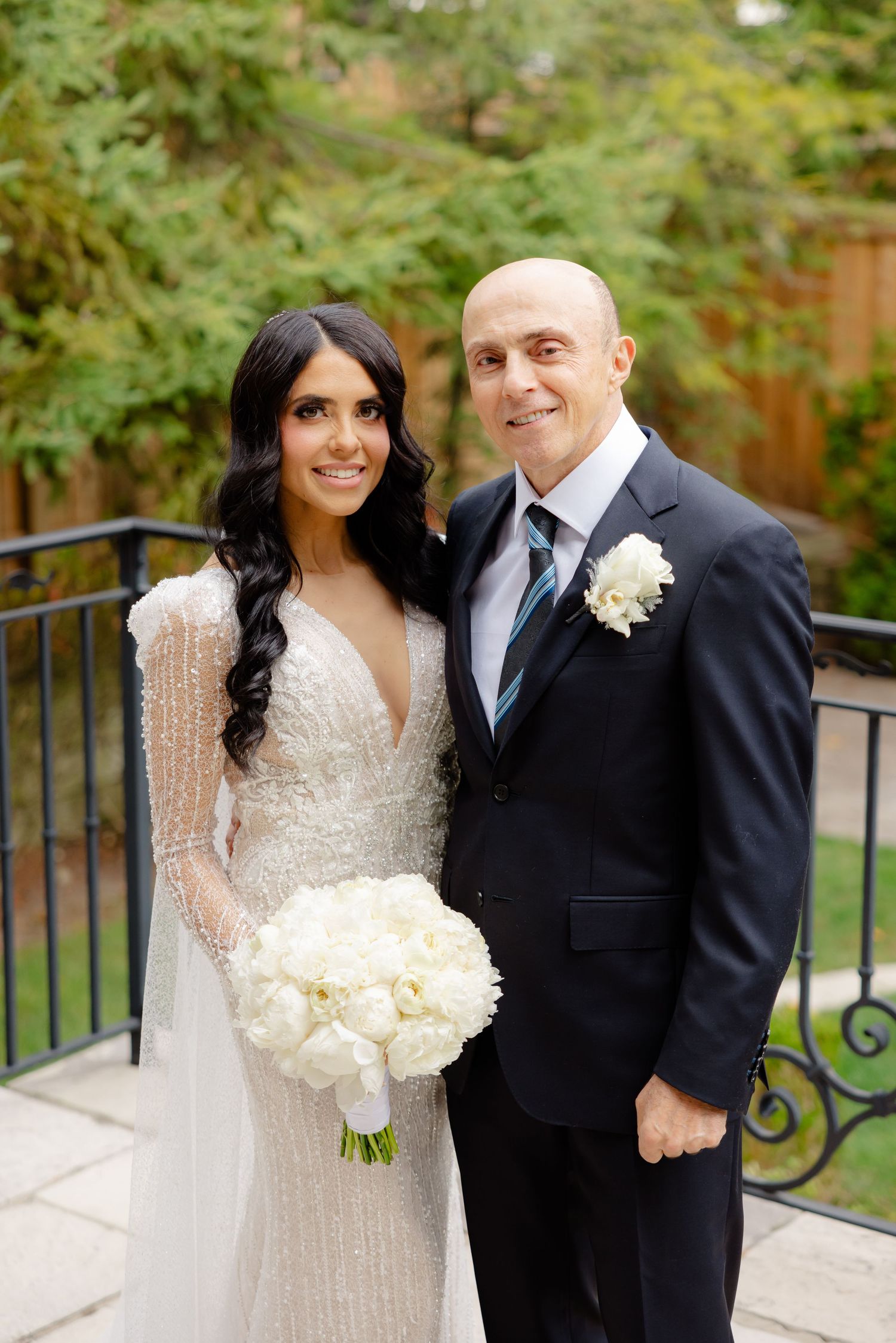 Beautiful wedding portrait featuring a sparkling gown and classic tuxedo against garden scenery.