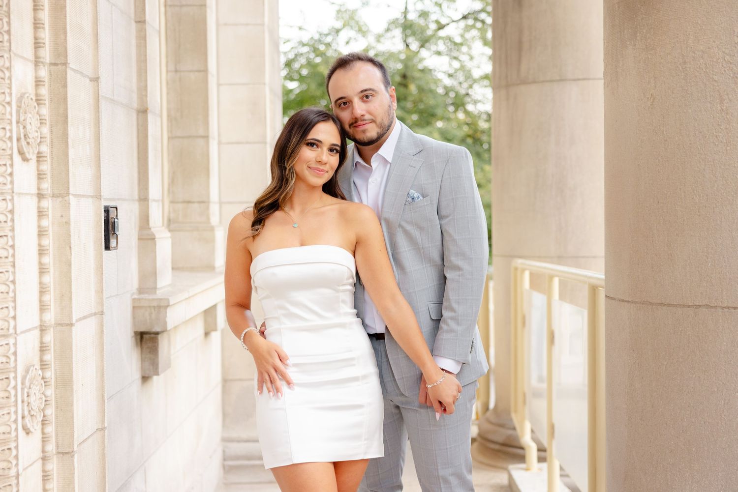 Fashionable couple poses together in an architectural setting with stone columns.