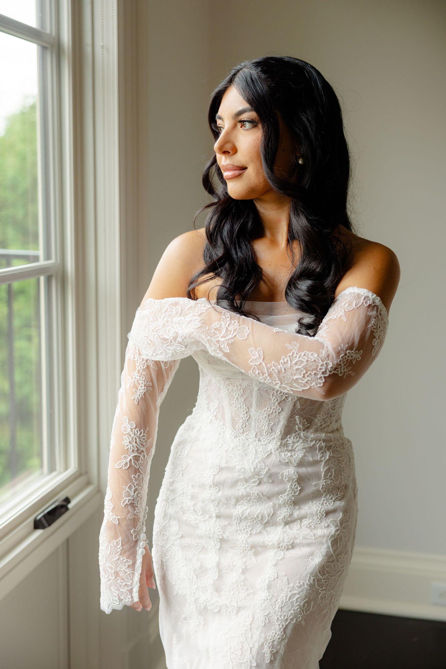 Off-shoulder bridal gown with intricate lace detailing displayed in a sunlit room.