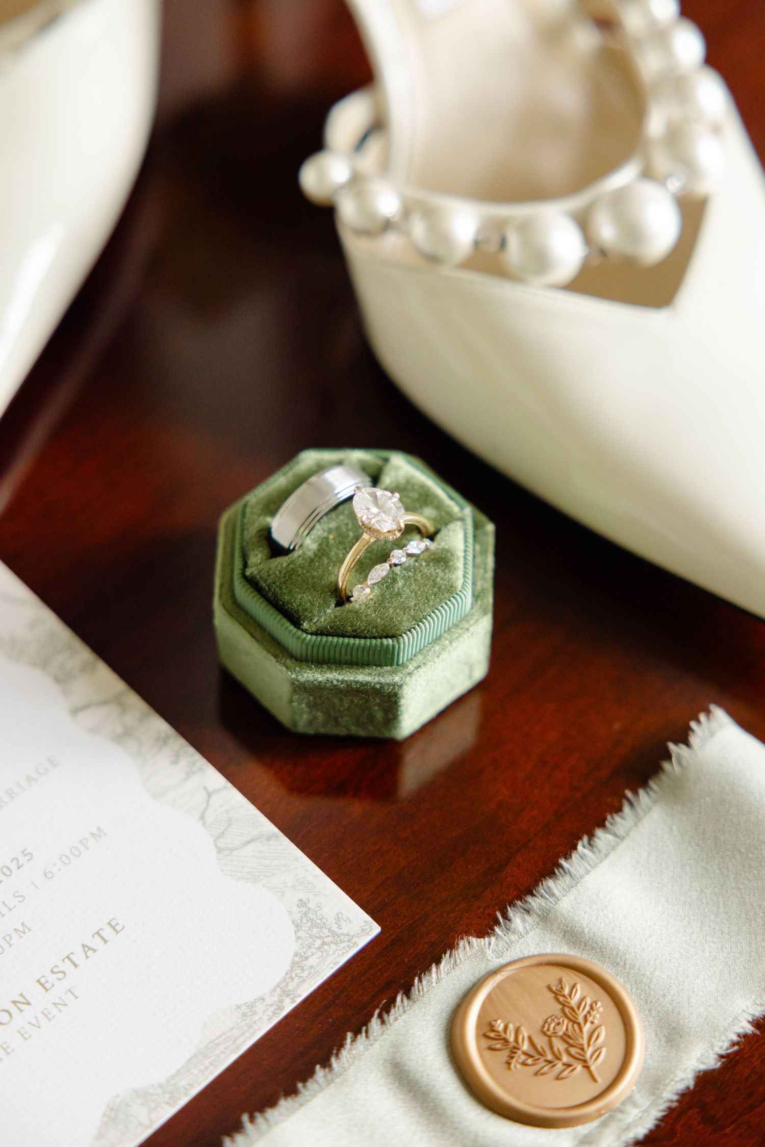Wedding details featuring a vintage green ring box, white shoes with pearl straps, and a gold wax seal on paper.