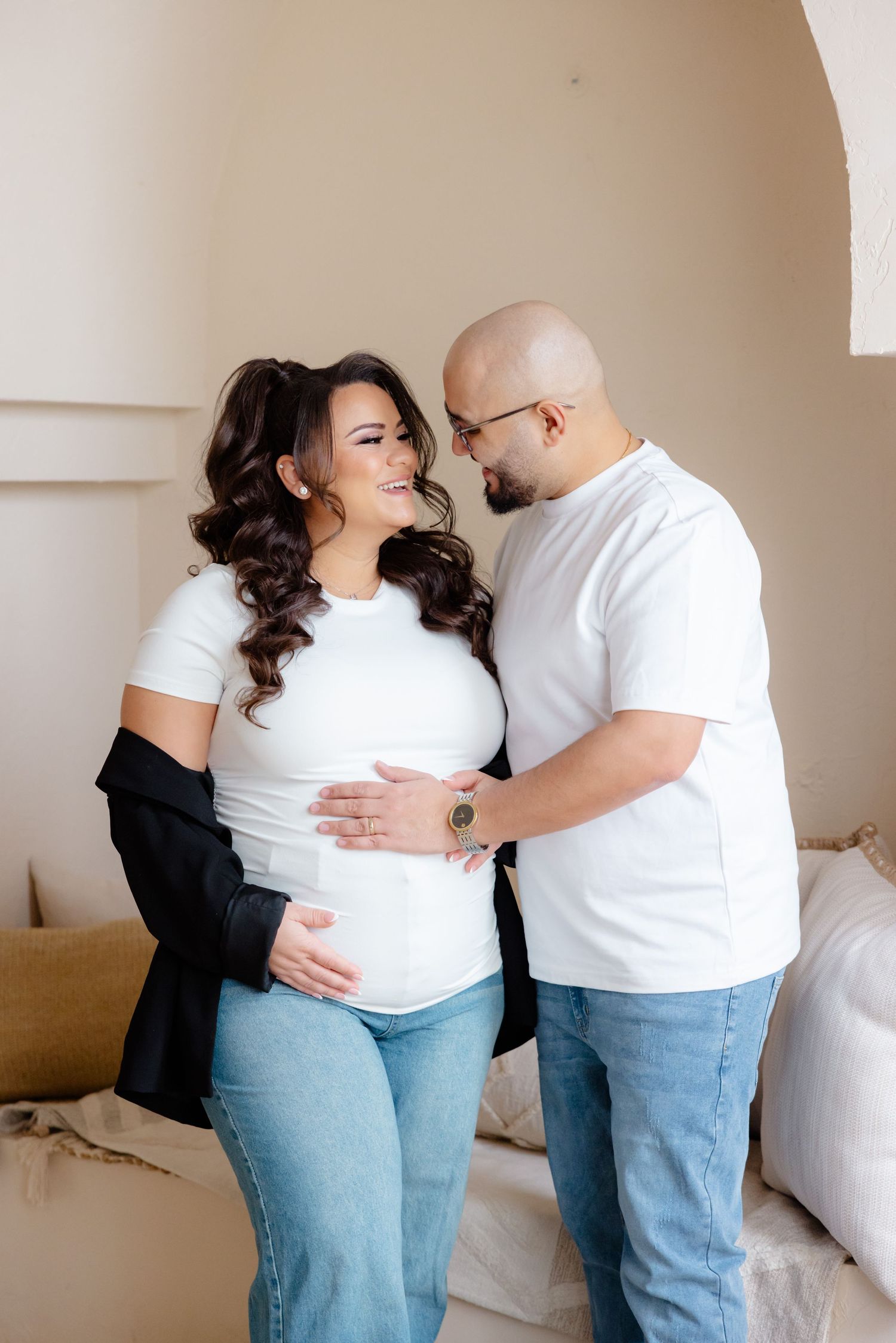 Expectant couple in matching white shirts share an intimate moment while cradling a baby bump together.