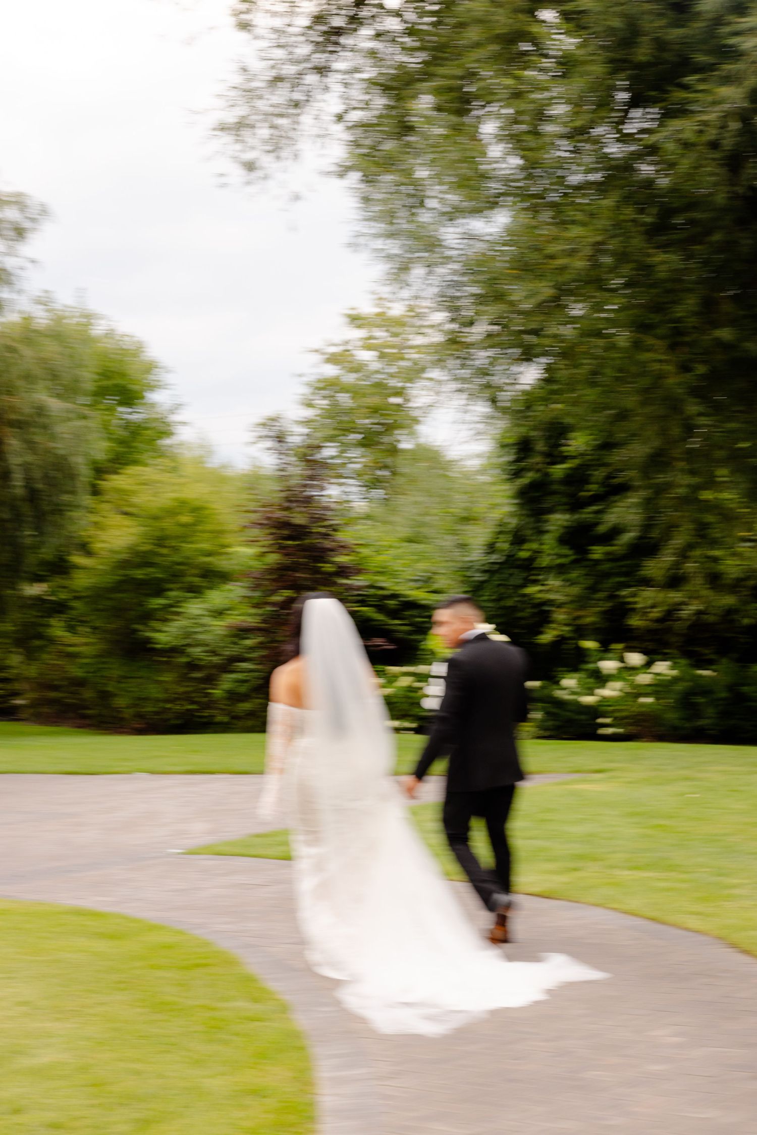 Newly married couple walking along a curved pathway through lush green gardens after their ceremony.