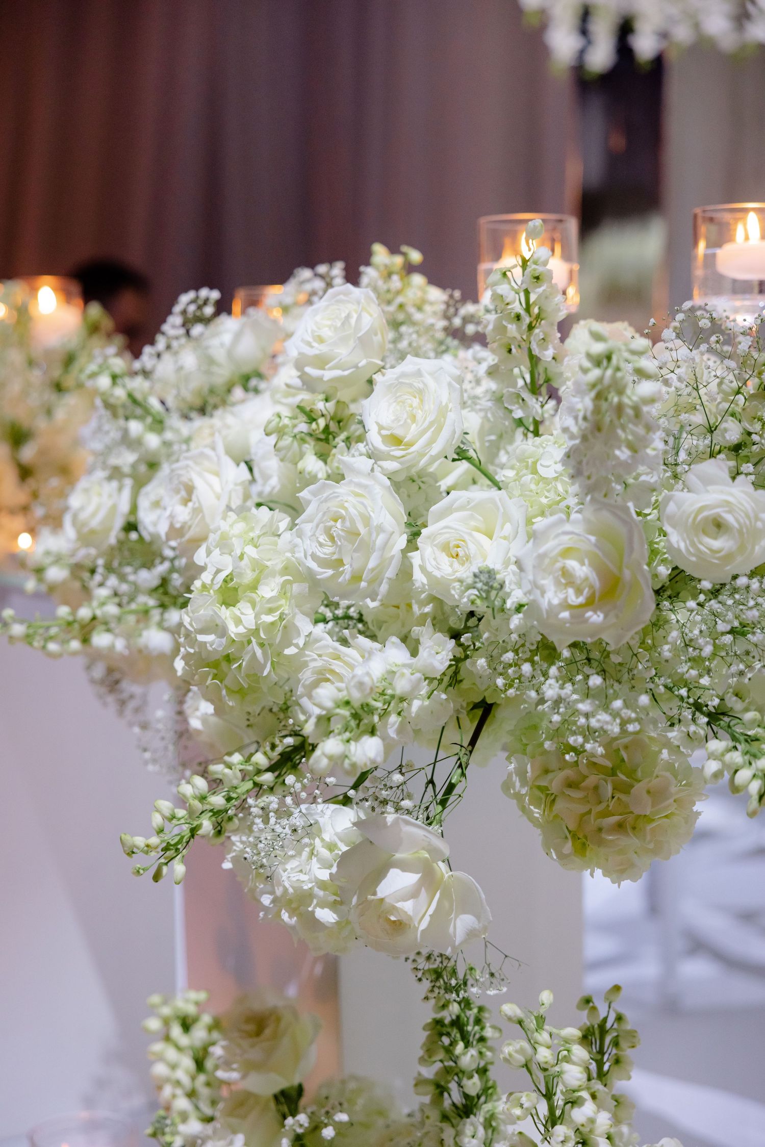Luxurious white rose and baby's breath floral arrangement with glowing candles for wedding reception decor.