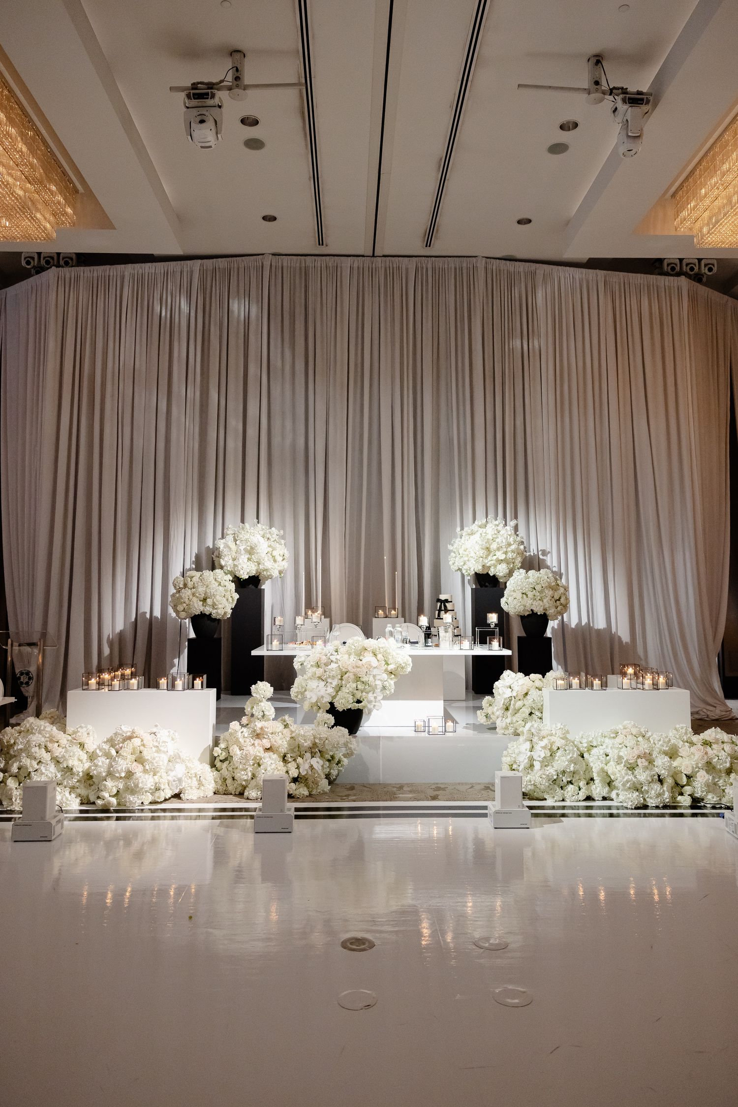 Elegant white wedding reception room with draped fabric walls and cascading floral centerpieces illuminated by soft lighting.