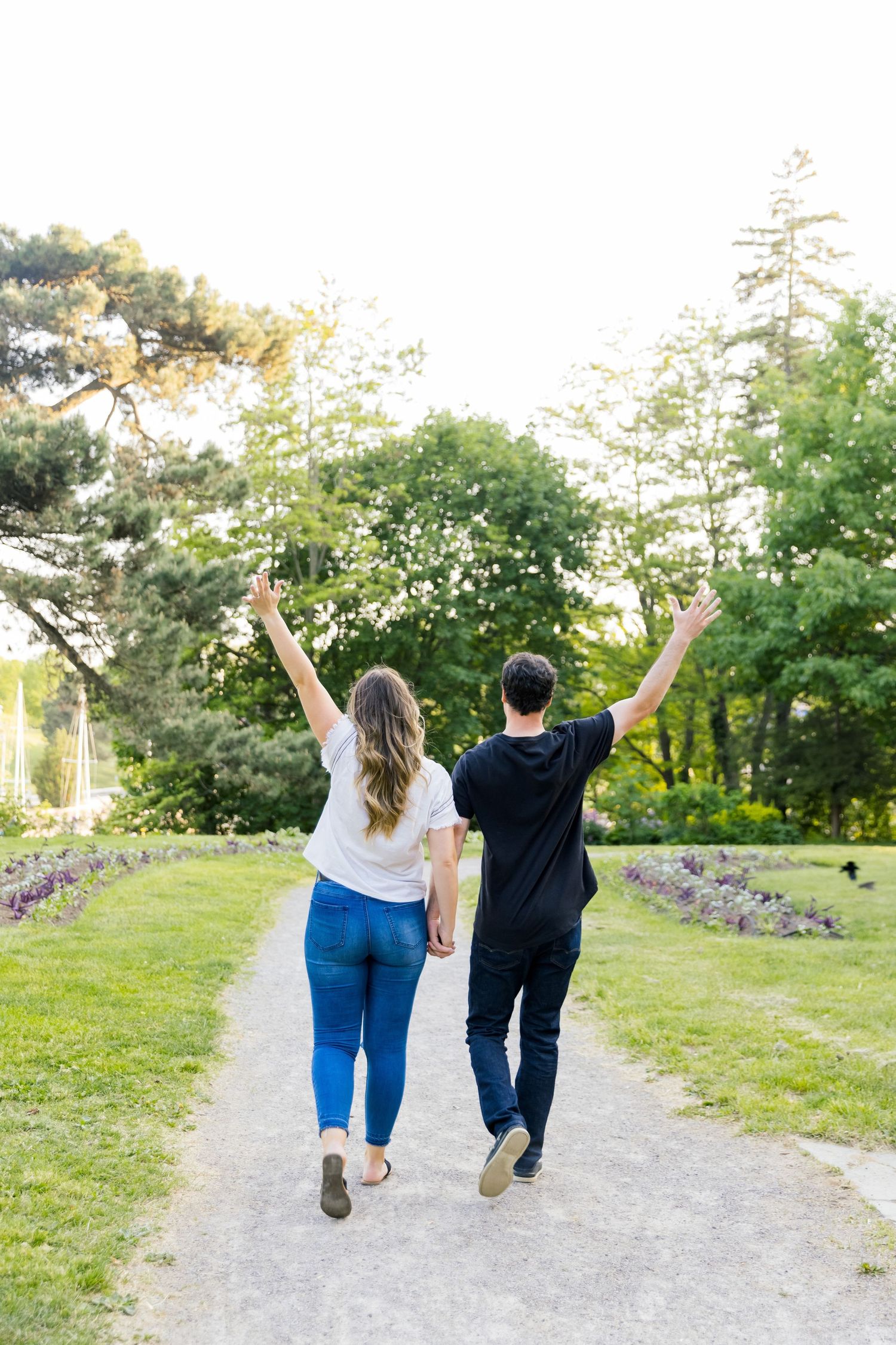 Couple walking away on a path with raised arms celebrating in a sunny garden setting.