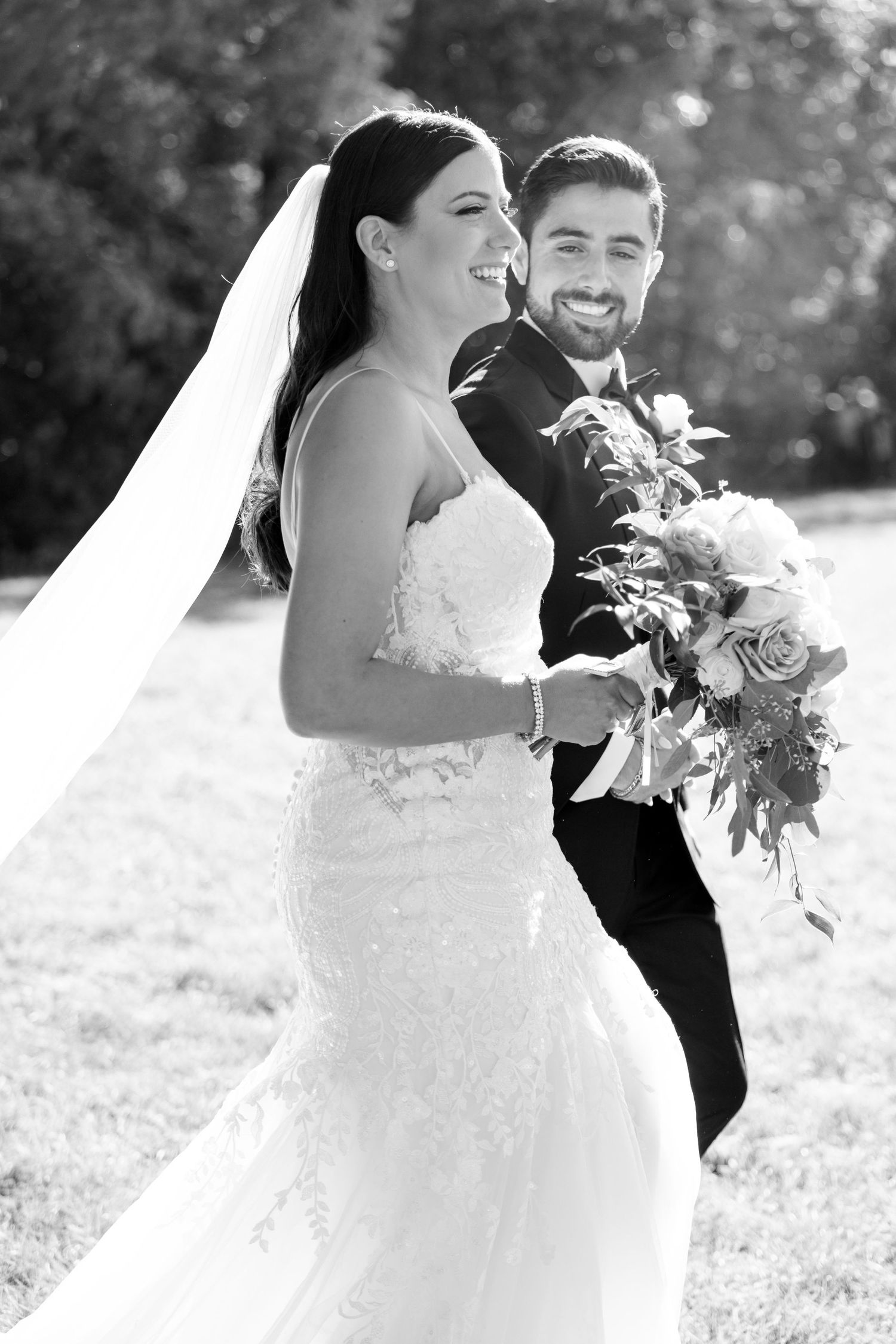 Black and white candid photo of couple laughing during outdoor wedding portraits.