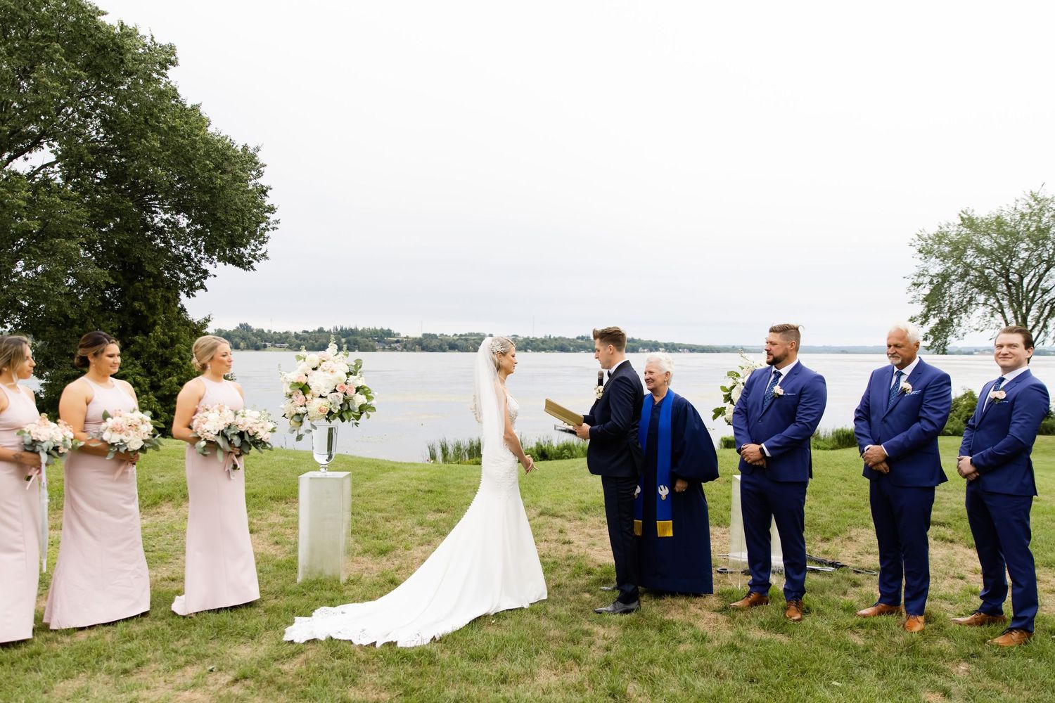 Lakeside wedding ceremony with groomsmen in navy suits and bridesmaids in blush dresses.