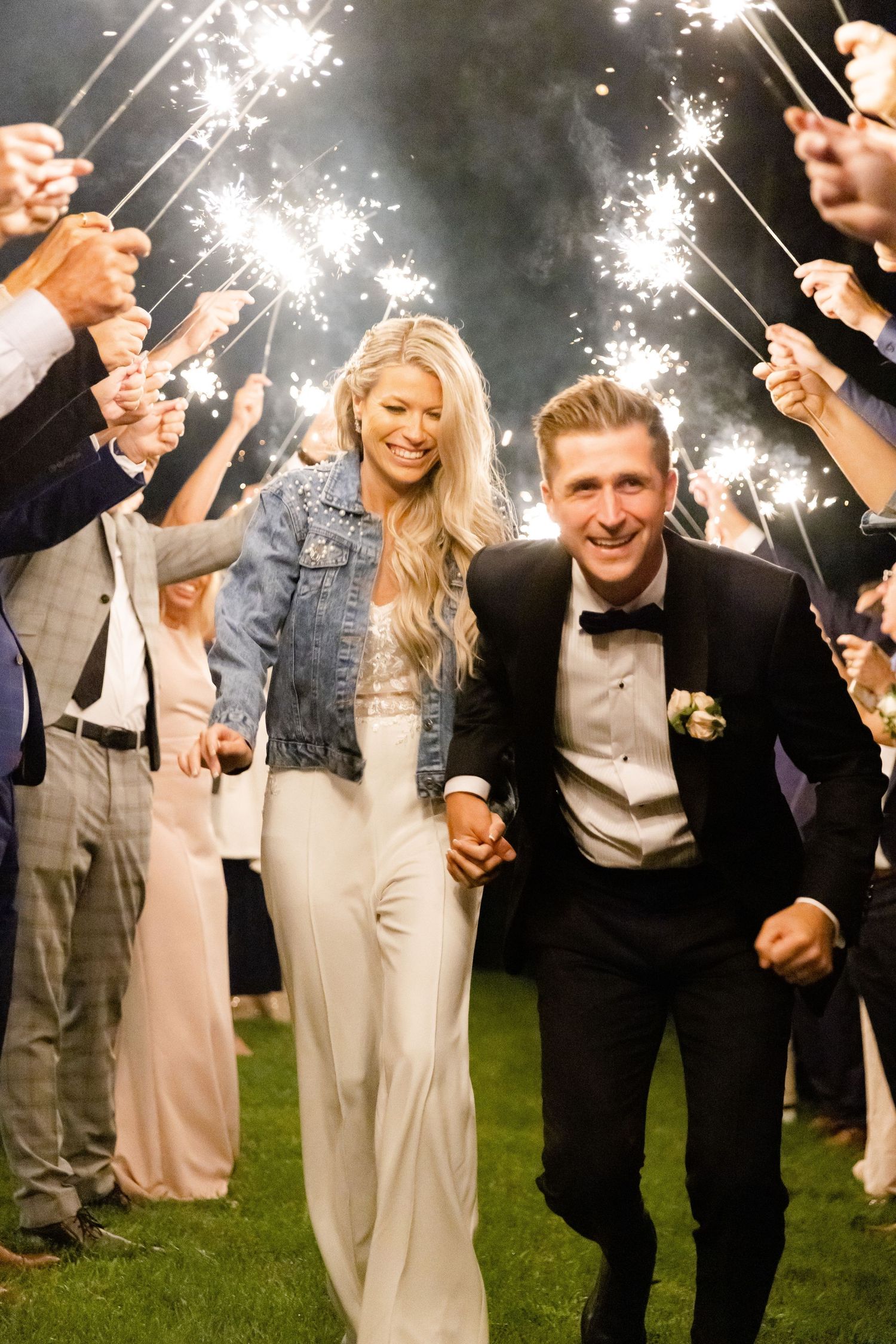 Joyful newlyweds run through sparkler tunnel during wedding reception exit.