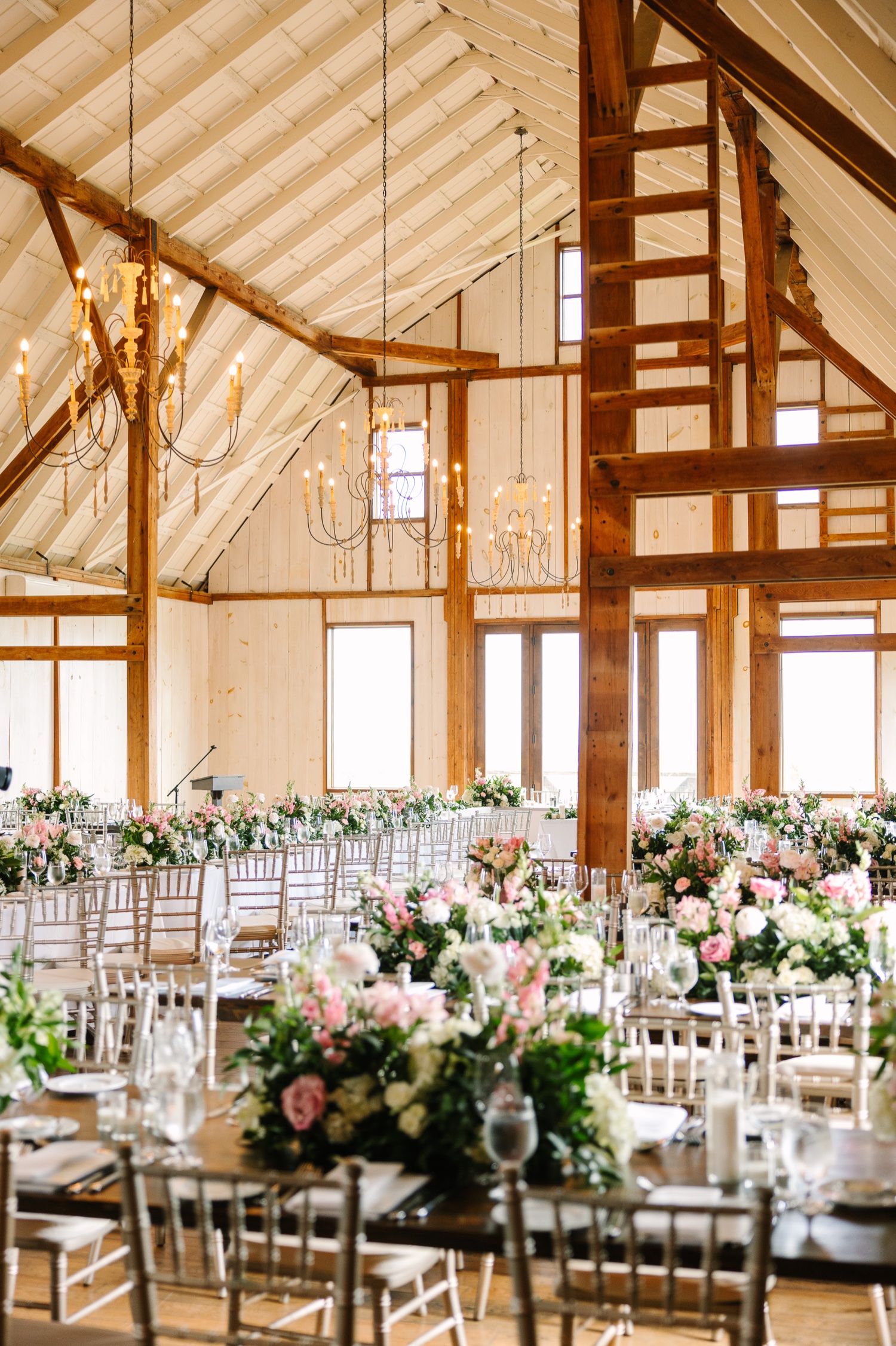 Light-filled barn venue with exposed wooden beams and elegant chandelier lighting.