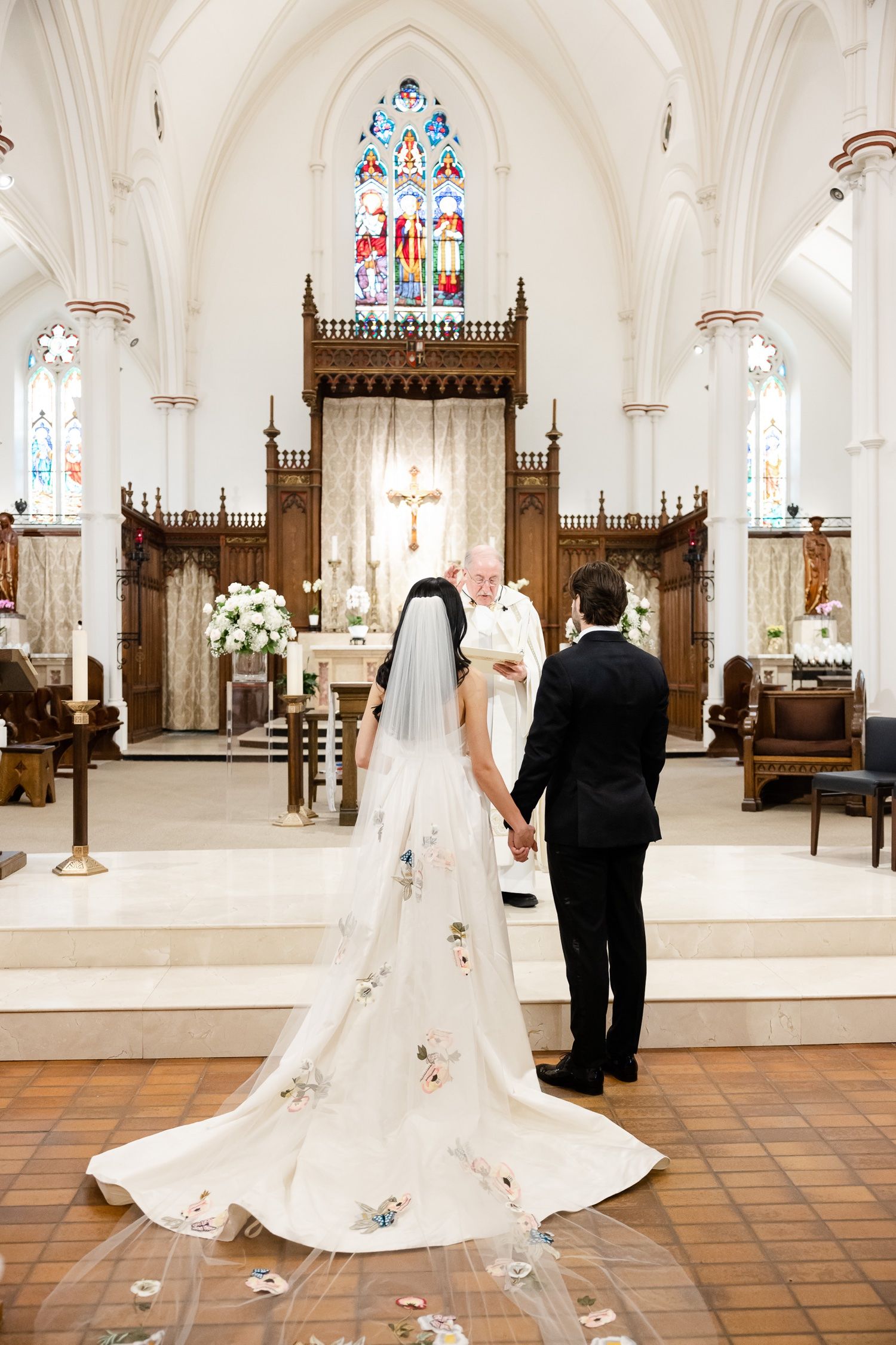A couple standing at the altar with an ornate wooden cross and stained glass window in background.